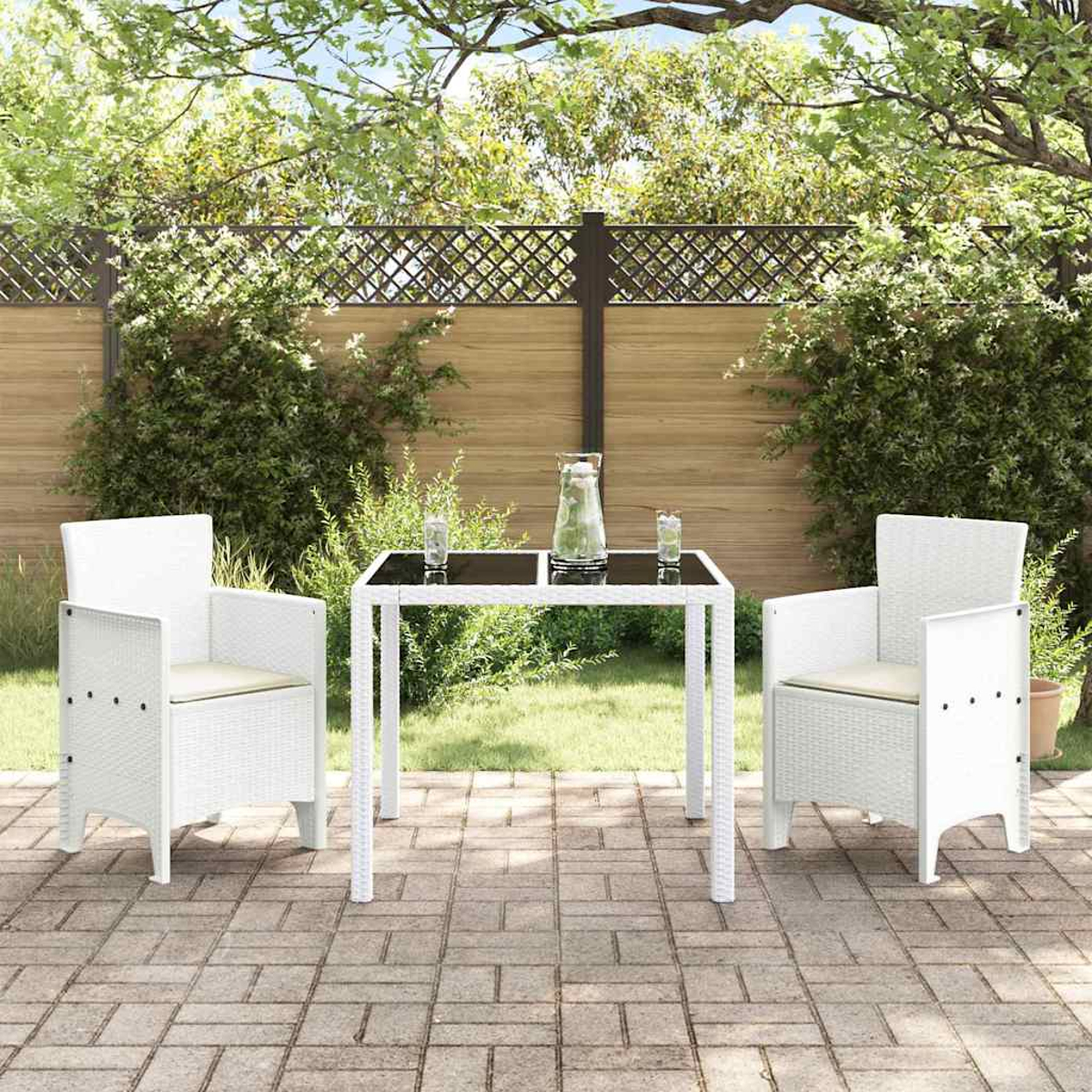 Eine Terrasse mit weißem Tisch und Stühlen. Eine Wasserkaraffe und Gläser stehen auf dem Tisch. Ein Zaun und Grünzeug sind im Hintergrund.