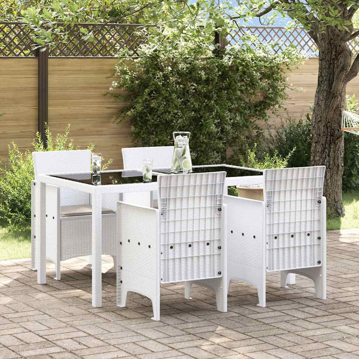 Ein weißes Terrassenset mit Glastisch und vier Stühlen. Auf dem Tisch stehen eine Kanne Wasser und Gläser. Es ist von Grün umgeben.