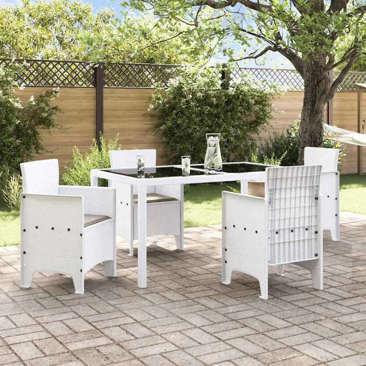 Weißer Tisch und Stühle auf einer Ziegelterrasse. Getränke stehen auf dem Tisch. Im Hintergrund ein Baum und ein Zaun.