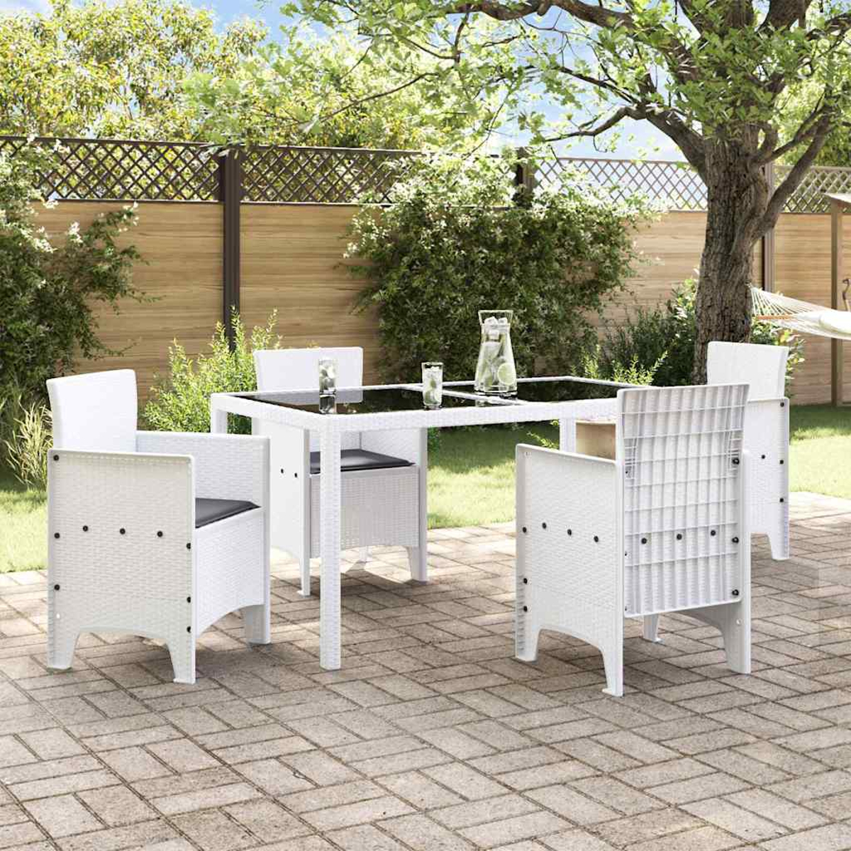 Ein weißes Terrassenset mit Tisch und Stühlen befindet sich in einem Garten. Ein Baum spendet Schatten. Ein Zaun und eine Hängematte sind sichtbar.