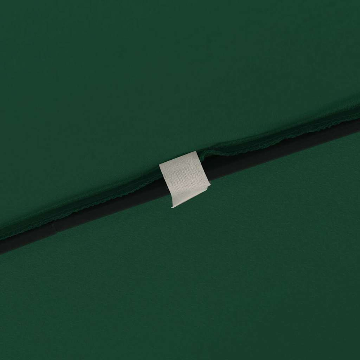Primer plano de tela verde con costura negra y etiqueta blanca. La tela tiene una textura suave.