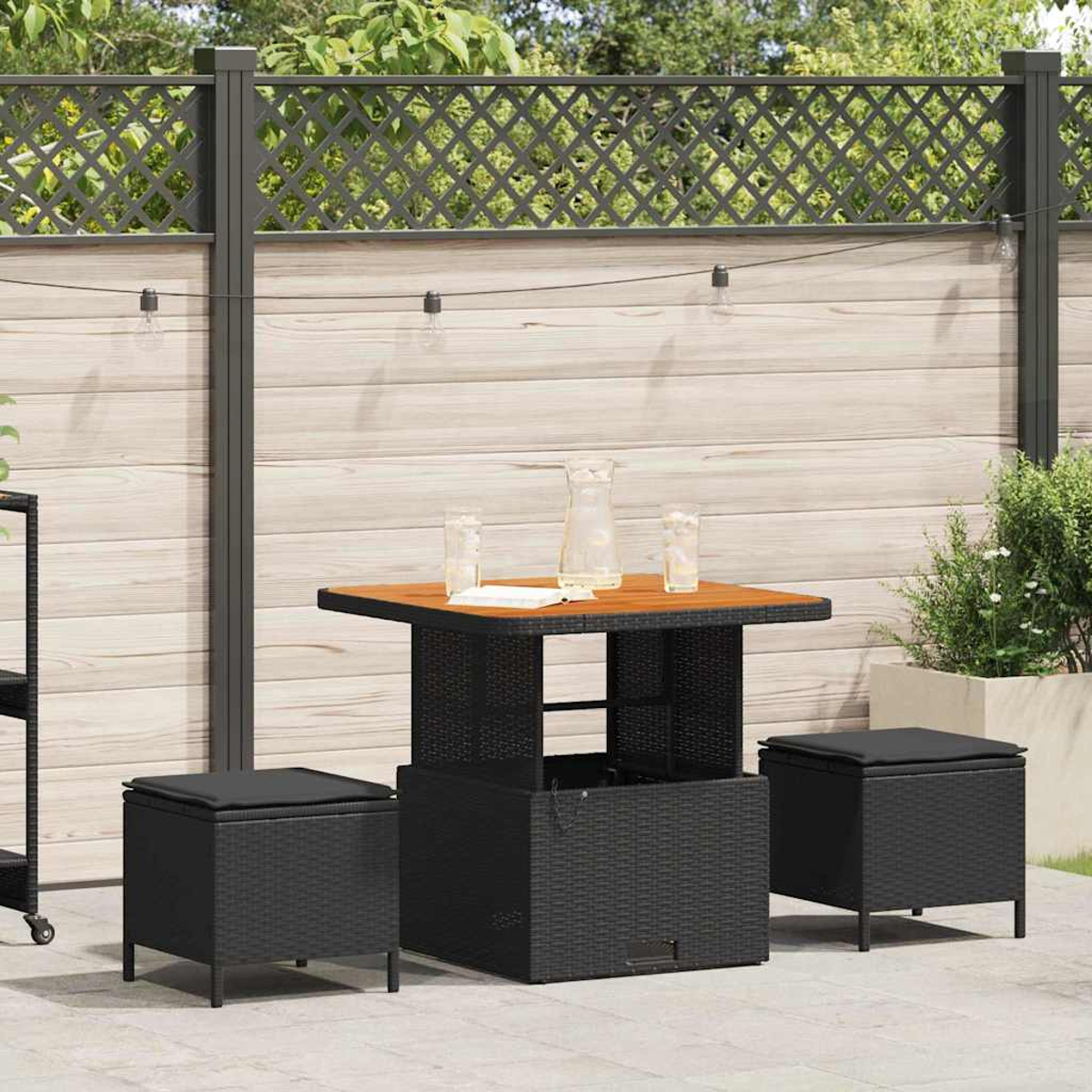 Terrassenset im Freien mit Tisch, zwei Hockern, Holzzaun und dekorativen Lichtern. Auf dem Tisch stehen ein Krug und Gläser.