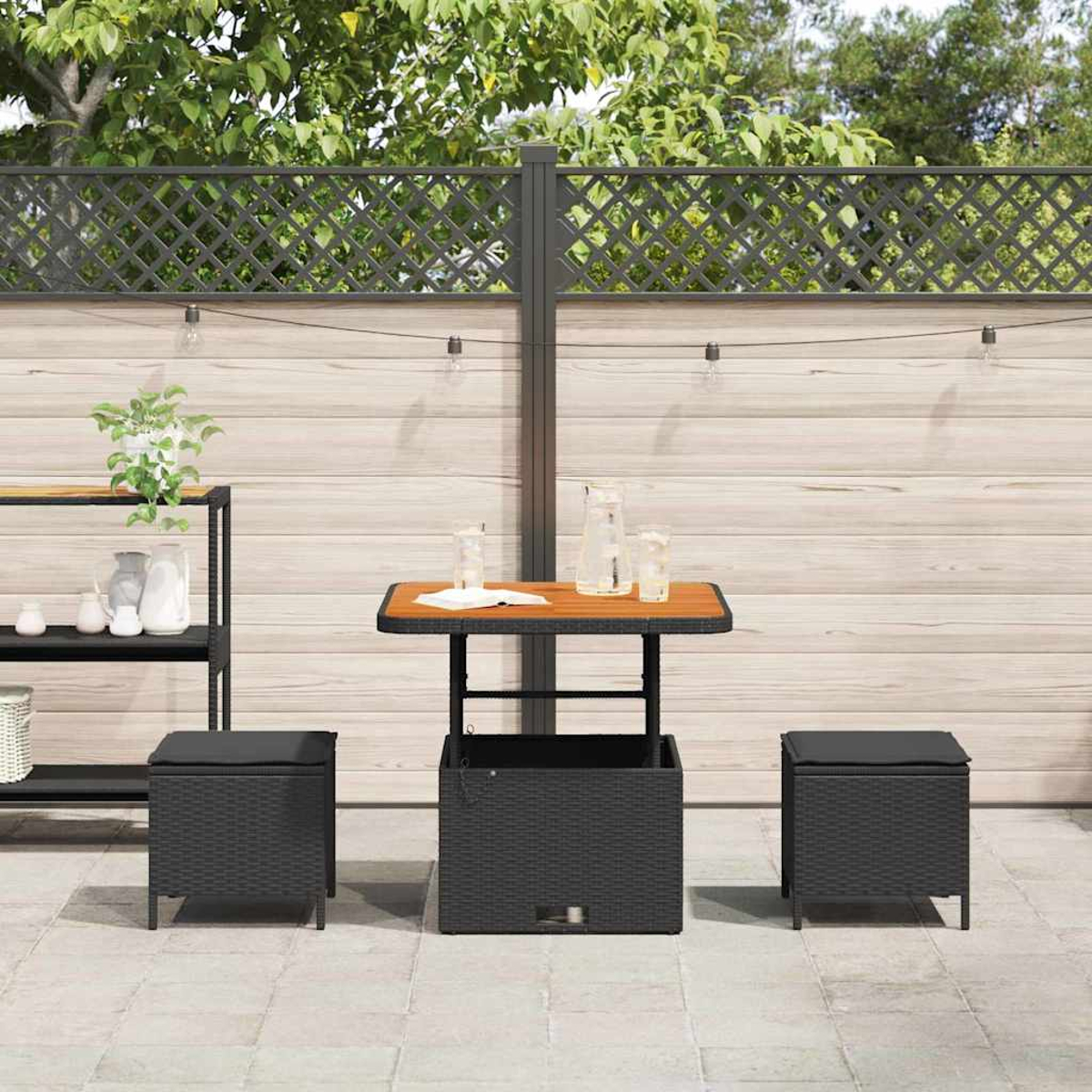 Outdoor-Terrassen-Set mit Tisch, zwei Ottomanen und einem dekorativen Zaun. Der Tisch hat eine Holzplatte und ist von Grün umgeben.