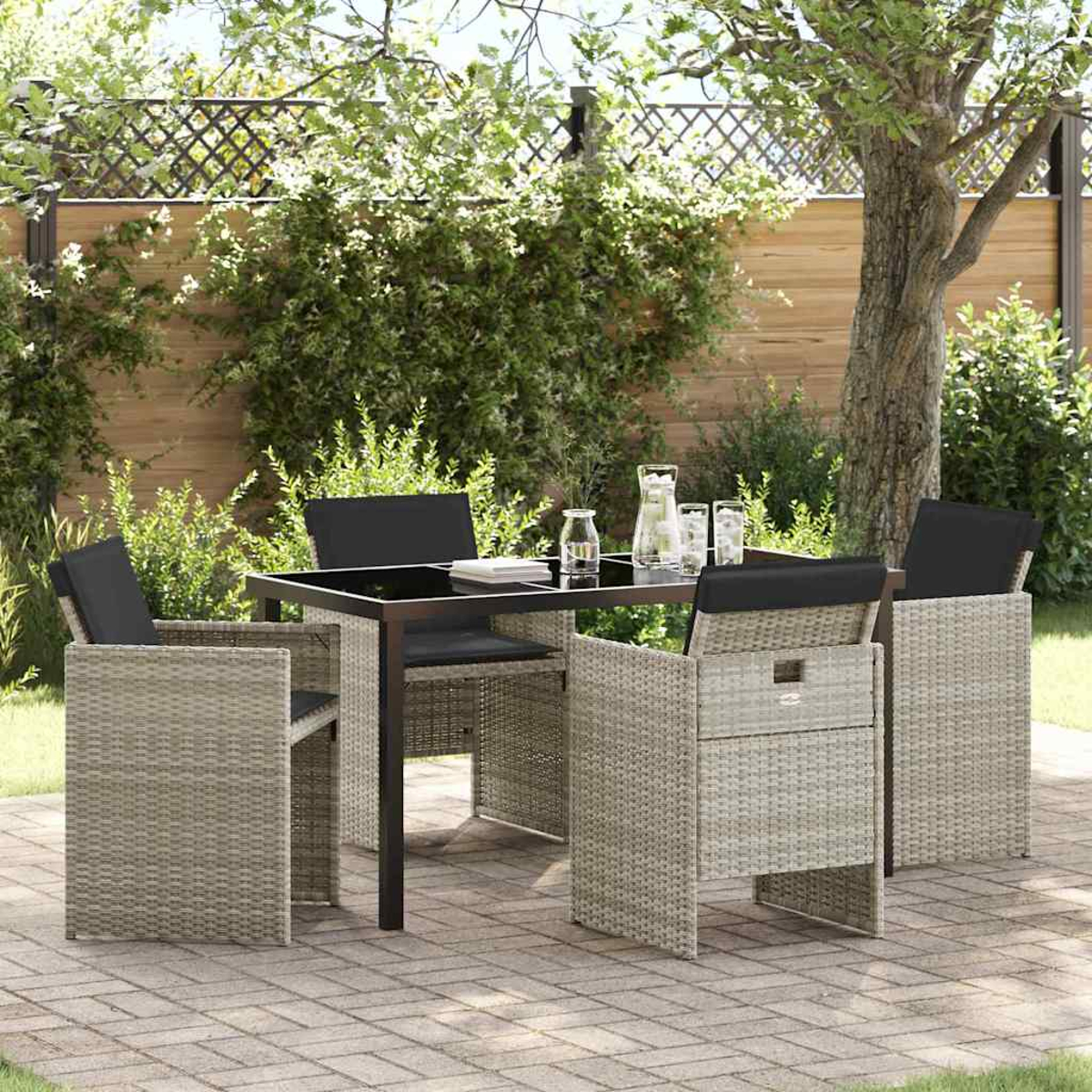 Set da pranzo all'aperto con tavolo nero, quattro sedie con cuscini neri e un bicchiere d'acqua, su un patio pavimentato.