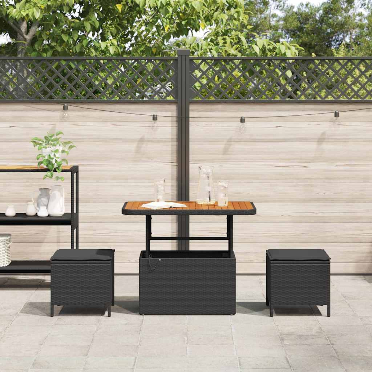 Szene auf der Terrasse mit Tisch, zwei Ottomanen und einer Aufbewahrungsbox. Im Hintergrund ein Holzzaun und Pflanzen.