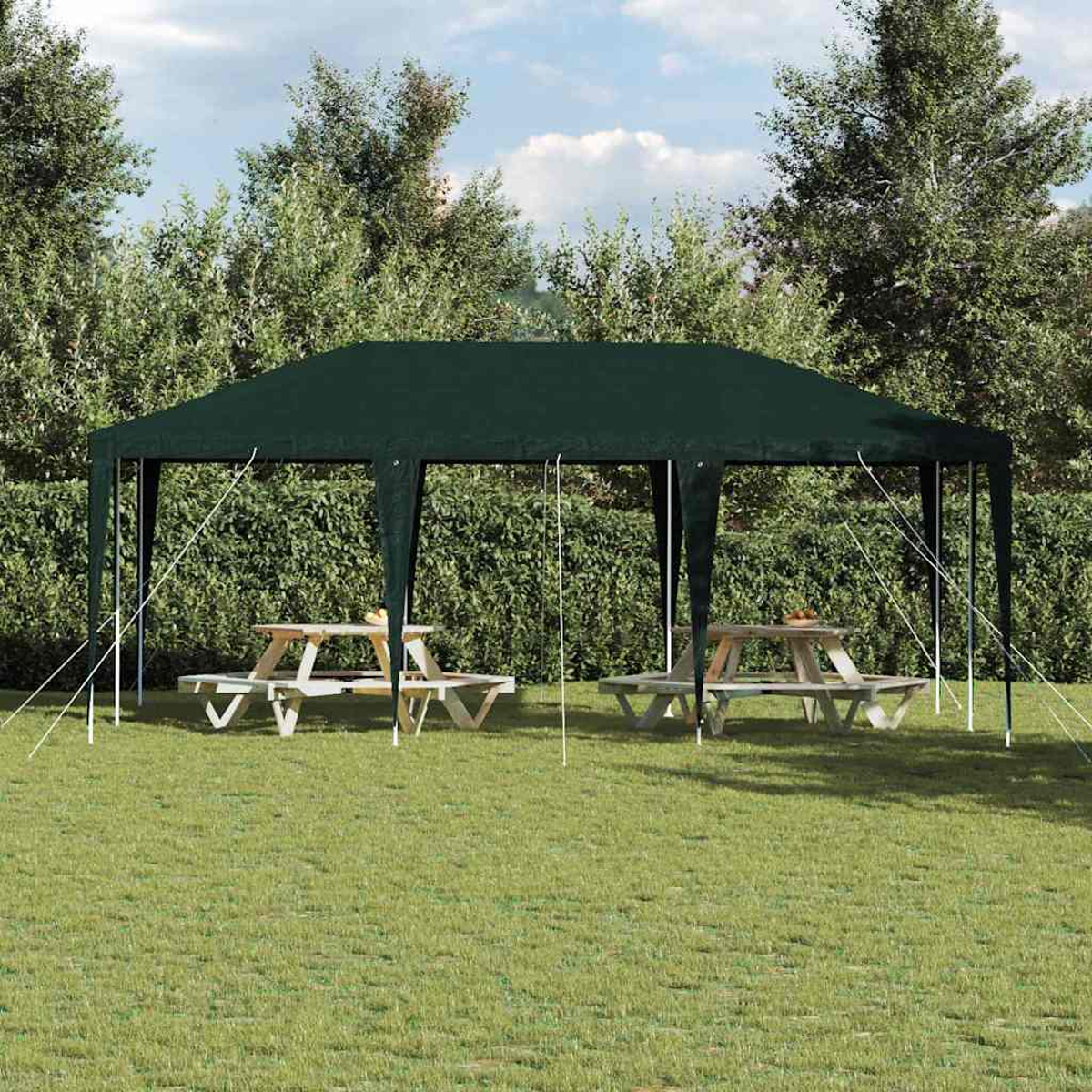 Ein grüner Pavillon steht auf Gras mit Picknicktischen im Inneren. Bäume und eine Hecke befinden sich im Hintergrund.