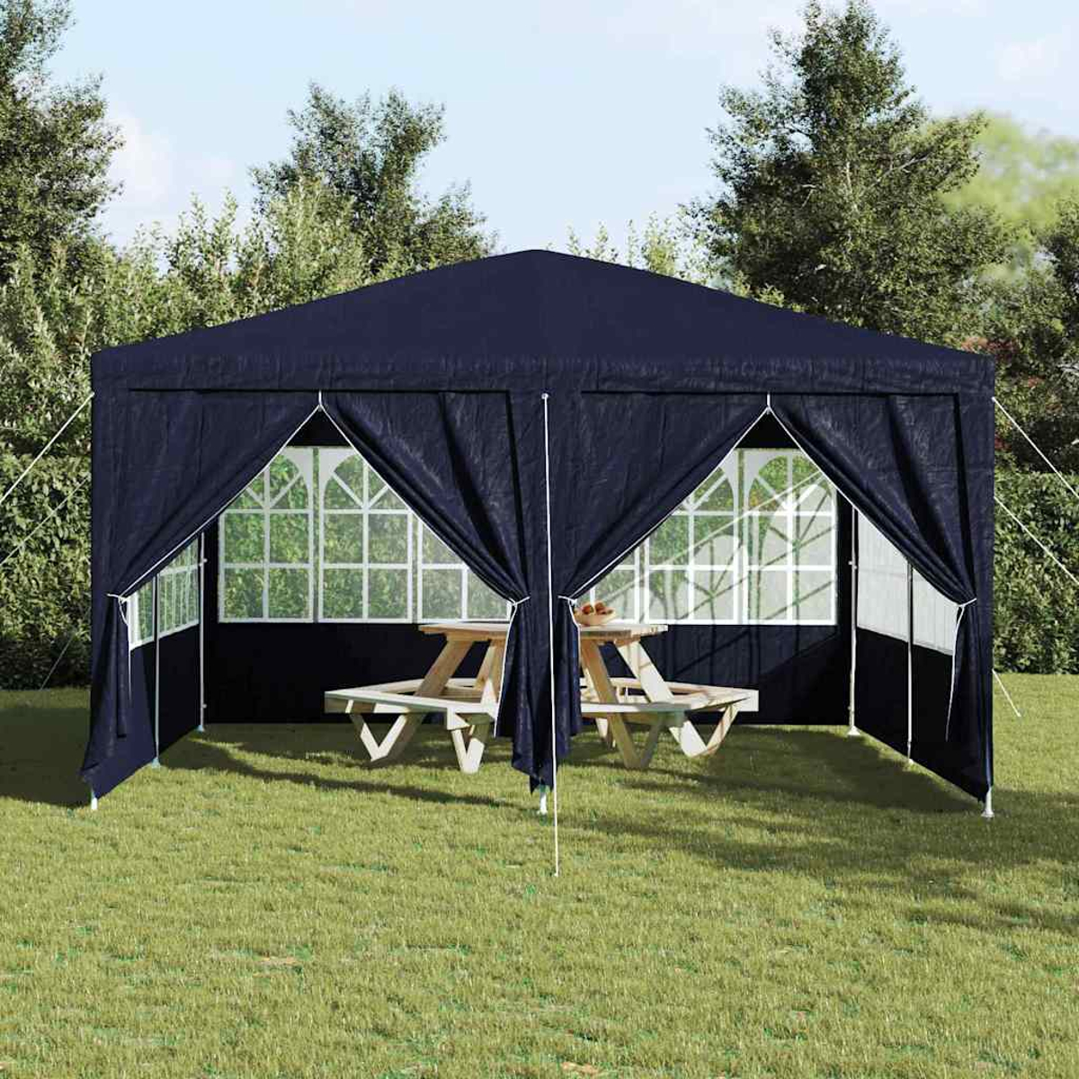 Ein dunkelblaues Gartenhaus steht auf Gras, mit Picknicktischen im Inneren. Bäume sind im Hintergrund.
