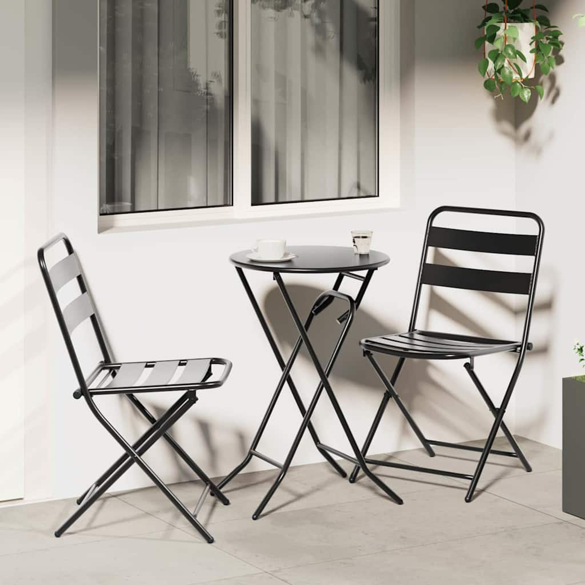 Schwarzes Metall-Terrassen-Set mit zwei Stühlen und einem kleinen Tisch. Ein weißes Fenster und eine Hängepflanze sind im Hintergrund.