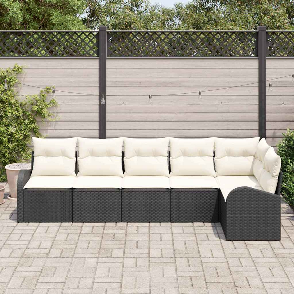 Outdoor-Ecksofa mit cremefarbenen Kissen auf einer gepflasterten Terrasse. Im Hintergrund befinden sich ein Holzzaun und Grün.