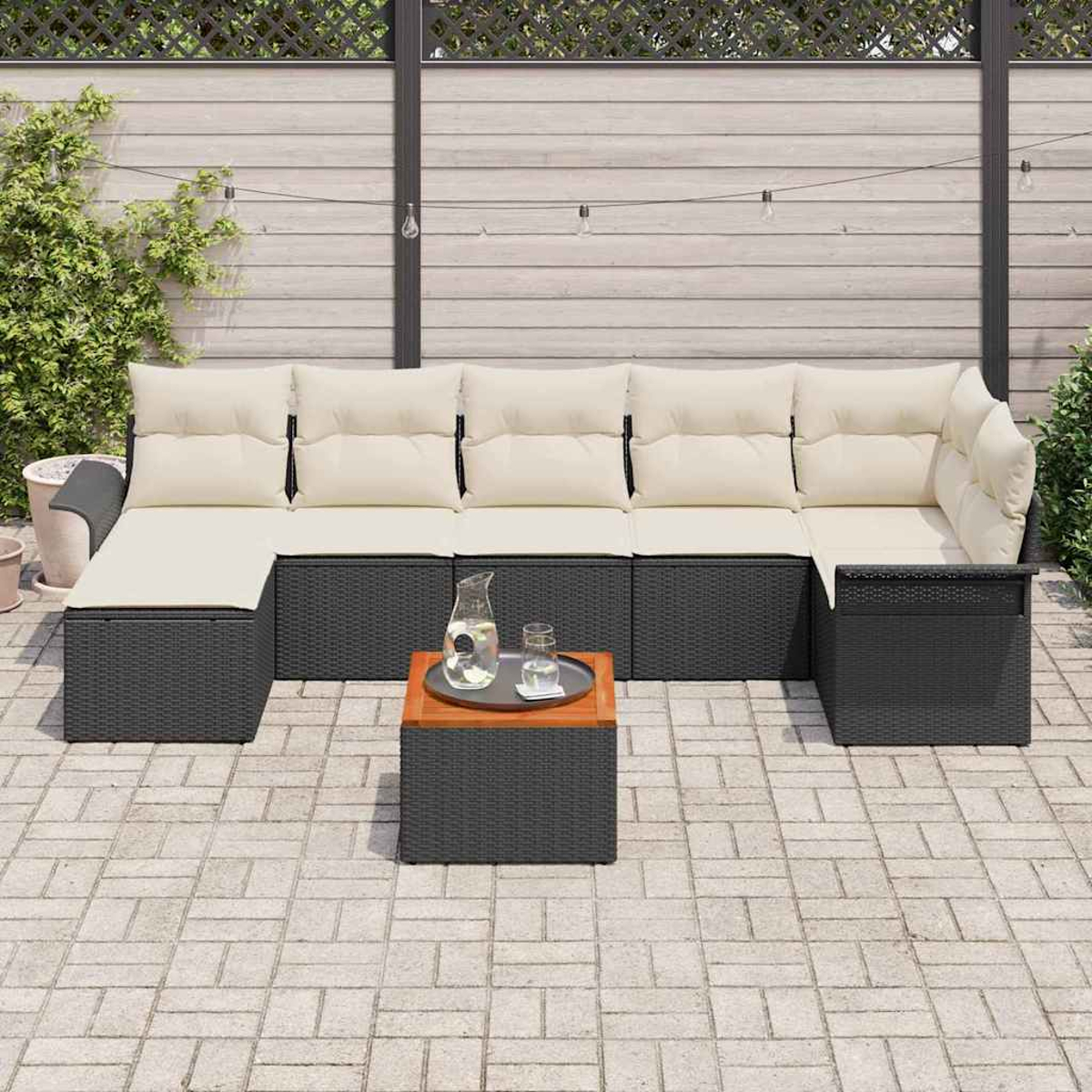 Outdoor-Ecksofa mit beigen Kissen, schwarzem Rahmen und einem kleinen Tisch mit Krug und Glas auf einer Terrasse.