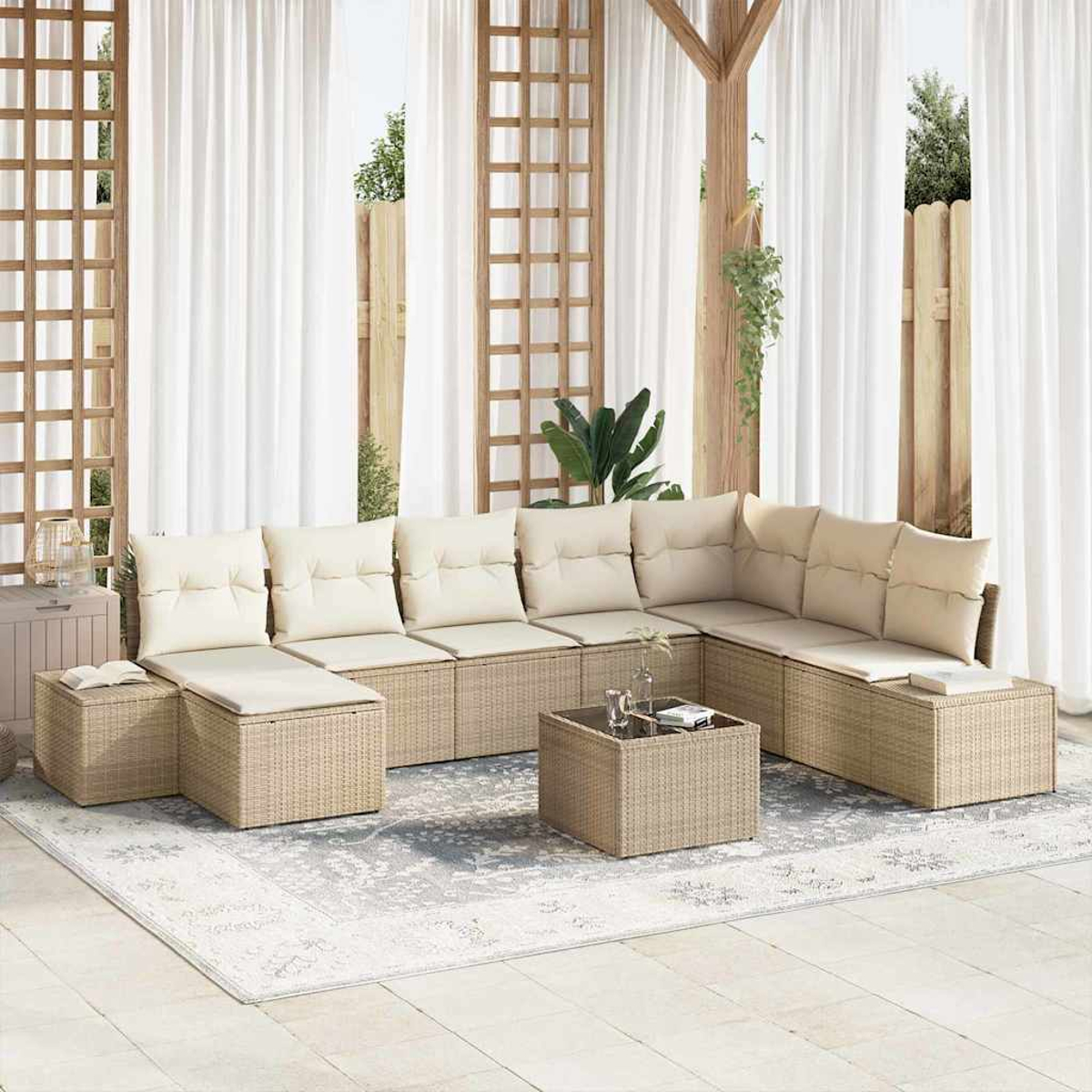 Outdoor-Sitzbereich mit beigen Kissen, Rattangeflechtmöbeln, einem Couchtisch und einem gemusterten Teppich, vor weißen Vorhängen.