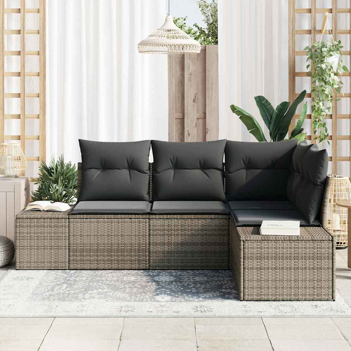 Ein Outdoor-Wicker-Sofa mit dunkelgrauen Kissen. Es steht auf einem Teppich, mit weißen Vorhängen, Pflanzen und einer Hängelampe im Hintergrund.