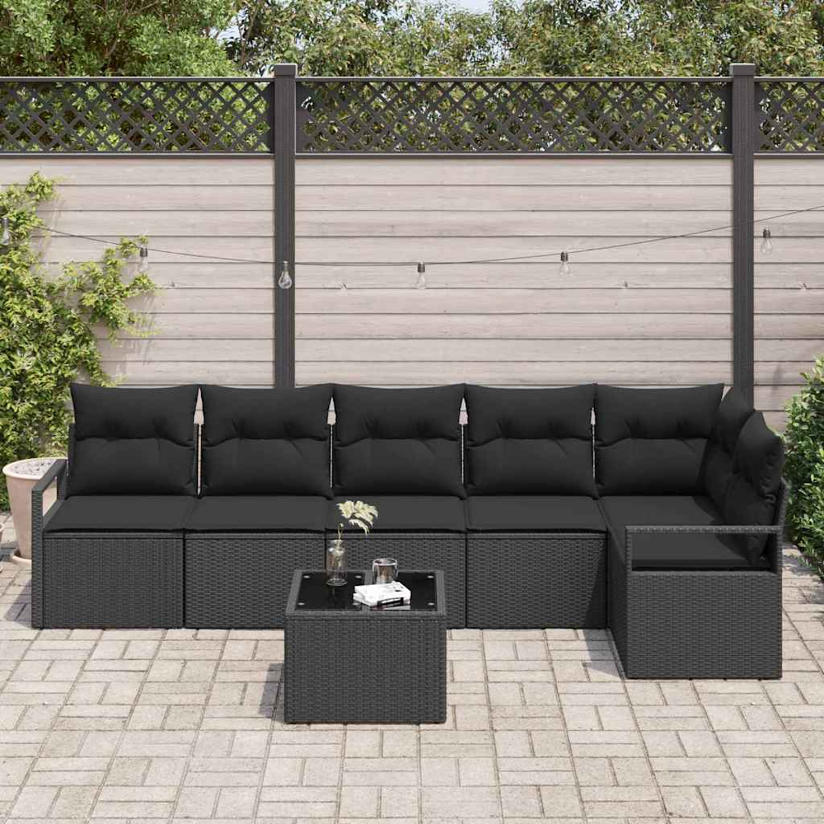 Outdoor-Ecksofa mit schwarzen Kissen, einem Couchtisch und einer Ziegelterrasse. Im Hintergrund befinden sich ein Zaun und Pflanzen.