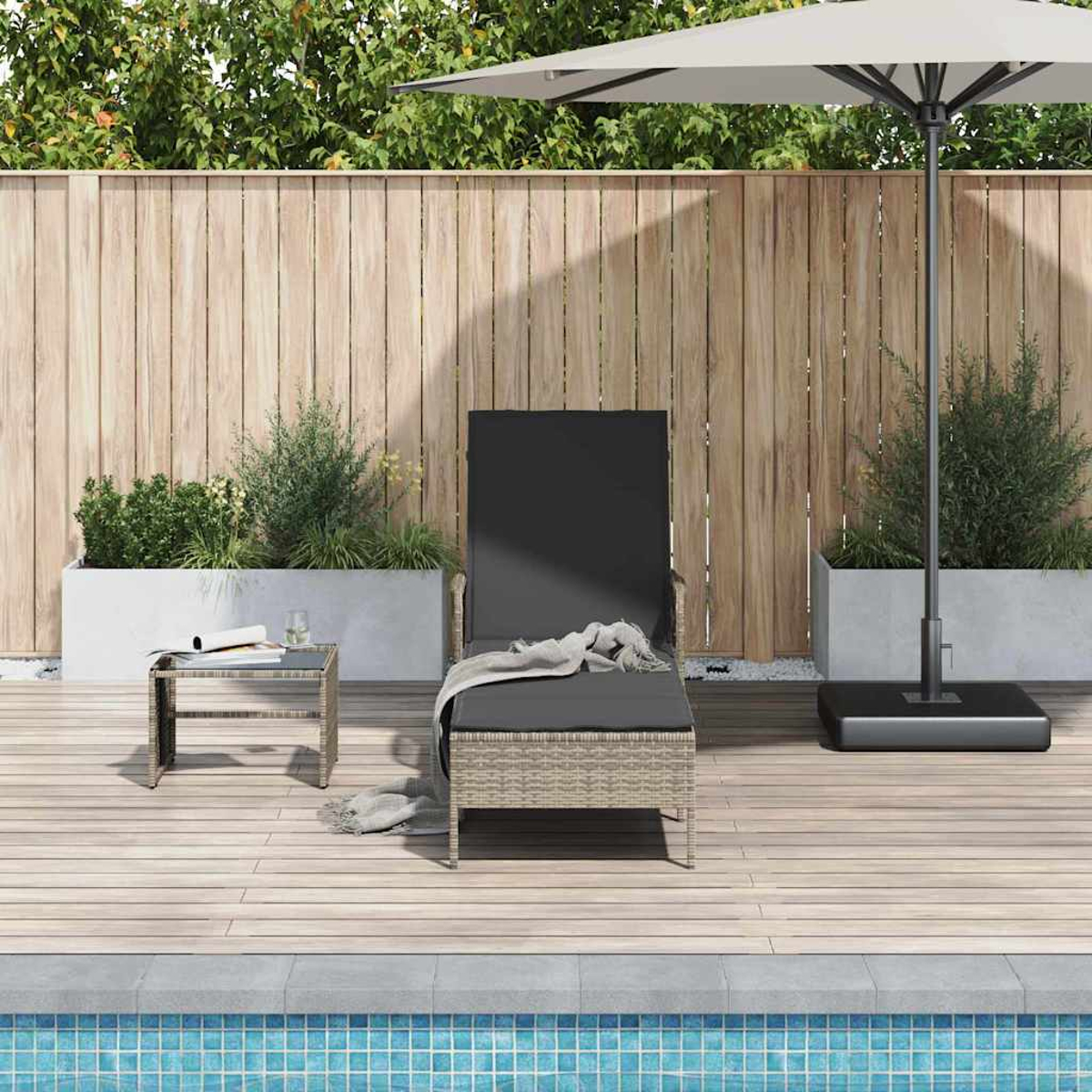 Eine Terrasse mit Liegestuhl, Tisch und Sonnenschirm in der Nähe eines Pools. Grün und ein Holzzaun im Hintergrund.