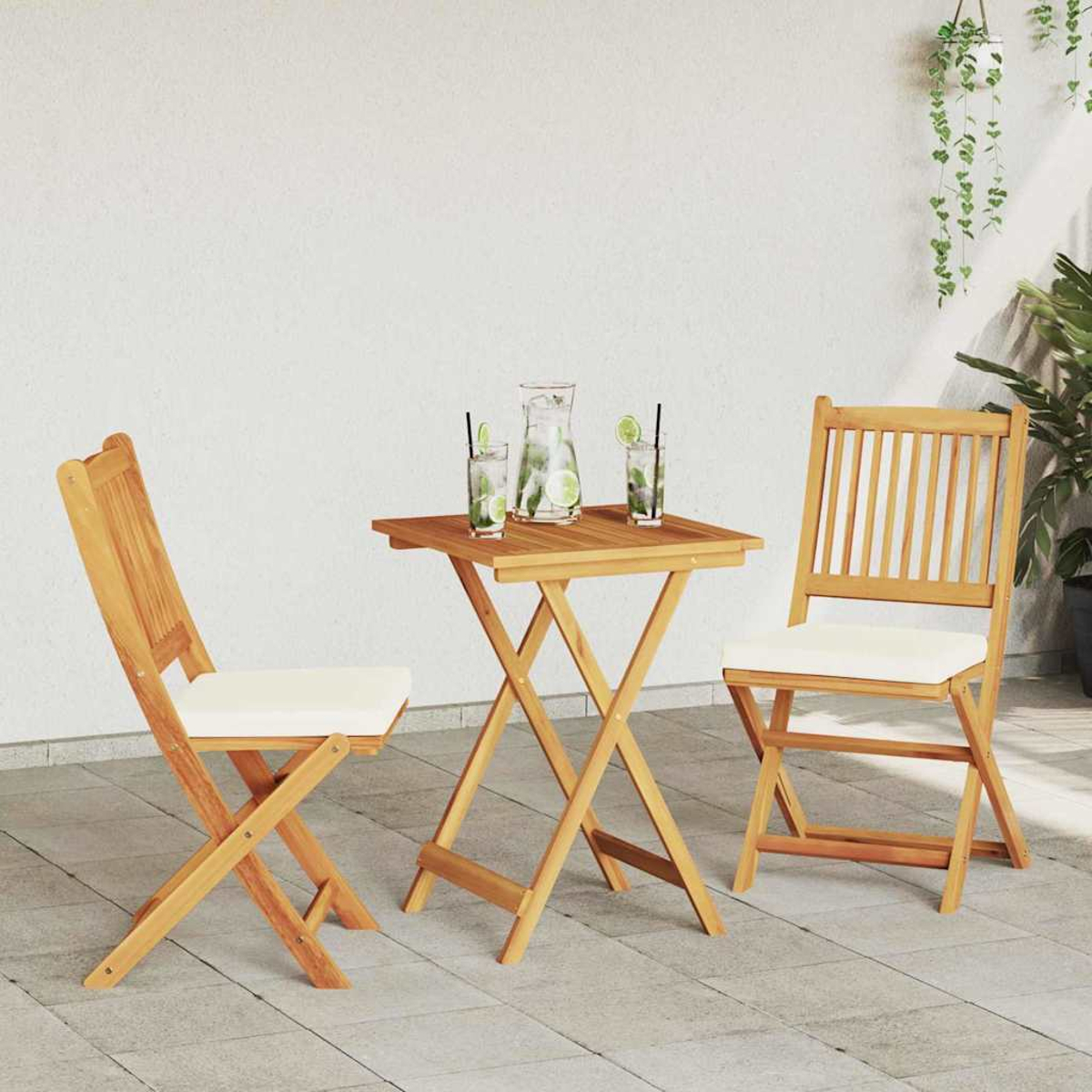 Holztisch und Stühle mit weißen Kissen. Getränke mit Limette und Eis stehen auf dem Tisch. Grüne Pflanzen hängen im Hintergrund.