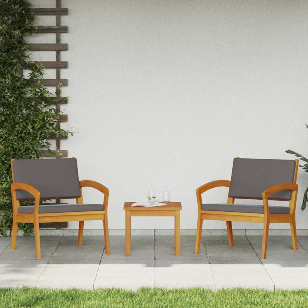 Dos sillas de madera con cojines grises y una mesa pequeña con vasos están en un patio. Se ve hierba verde.
