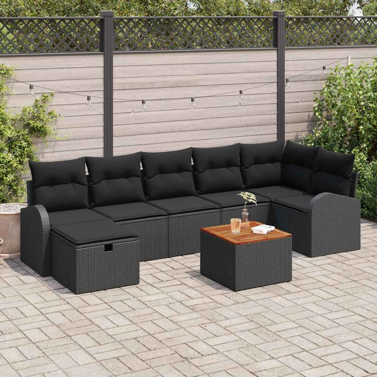 Gartensofa mit schwarzen Kissen und einem kleinen quadratischen Tisch. Im Hintergrund ein Holzzaun und etwas Grün.