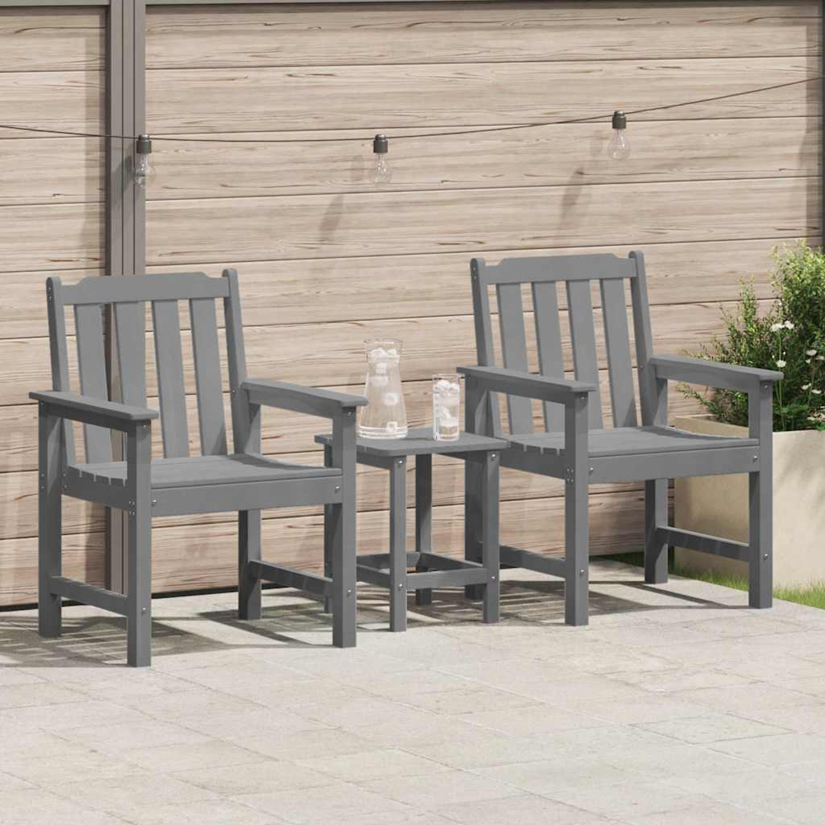 Zwei graue Stühle und ein kleiner Tisch mit Wassergläsern stehen auf einer Terrasse. Im Hintergrund befindet sich ein Holzzaun mit Lichterketten.