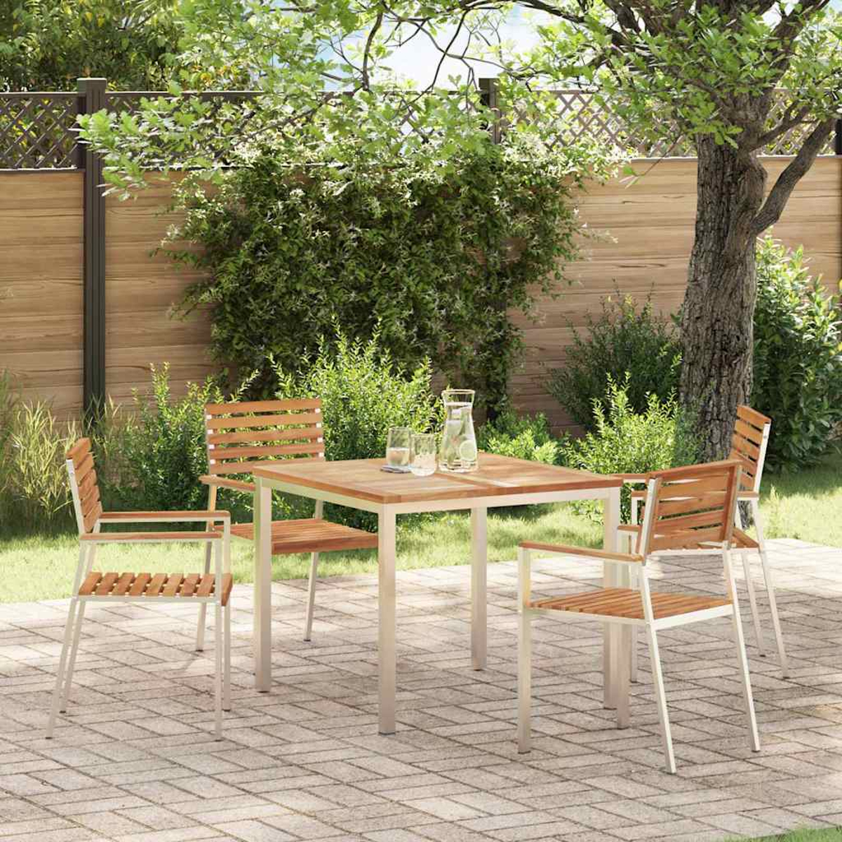 Ein Holztisch und Stühle auf einer Terrasse, umgeben von Grün und einem Holzzaun. Auf dem Tisch stehen ein Krug und Gläser.