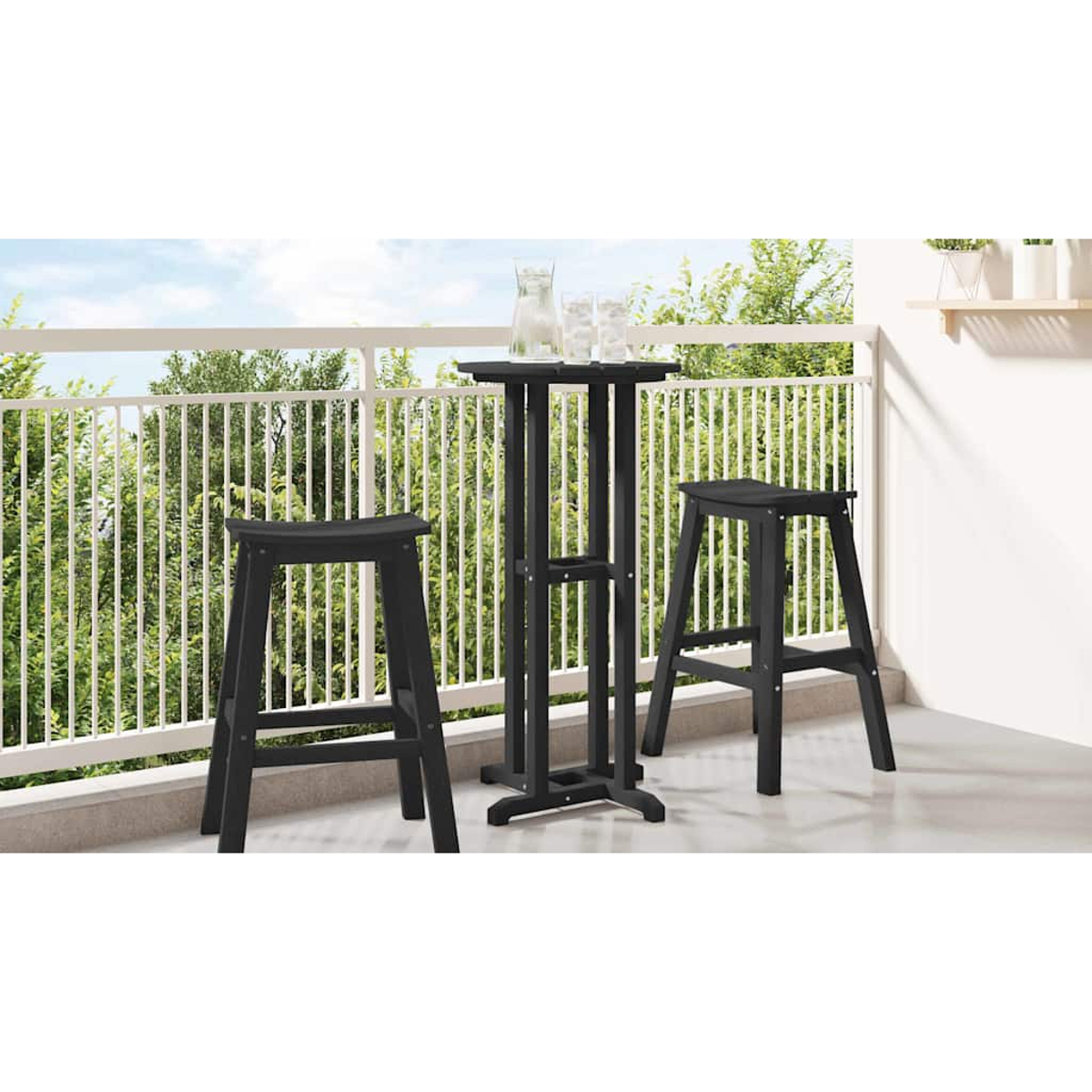 Una mesa de bar negra y dos taburetes en un balcón. Un vaso de agua y una jarra están en la mesa. Árboles verdes al fondo.