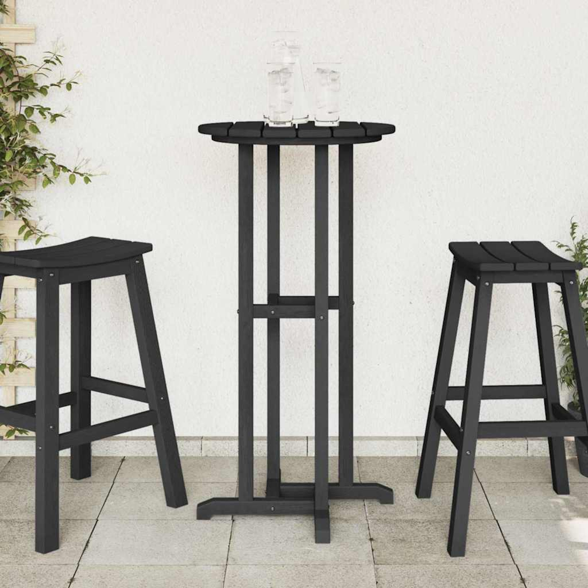Escena al aire libre con mesa de bar negra, dos taburetes y dos vasos. Fondo de pared blanca con plantas trepadoras a la izquierda.