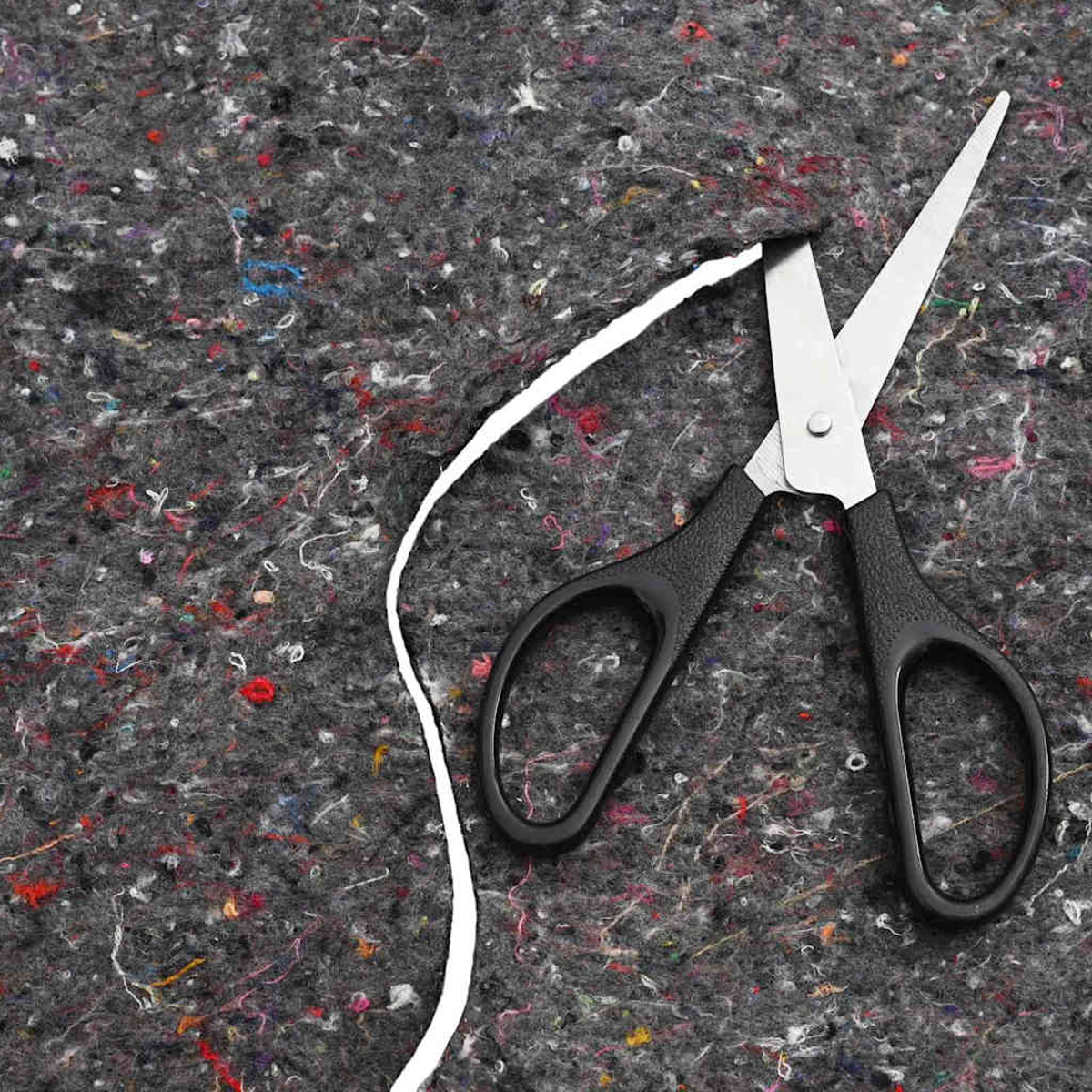 Schere schneidet einen weißen Faden auf einem grauen, mehrfarbigen Textil. Die Schere hat schwarze Griffe und silberne Klingen.