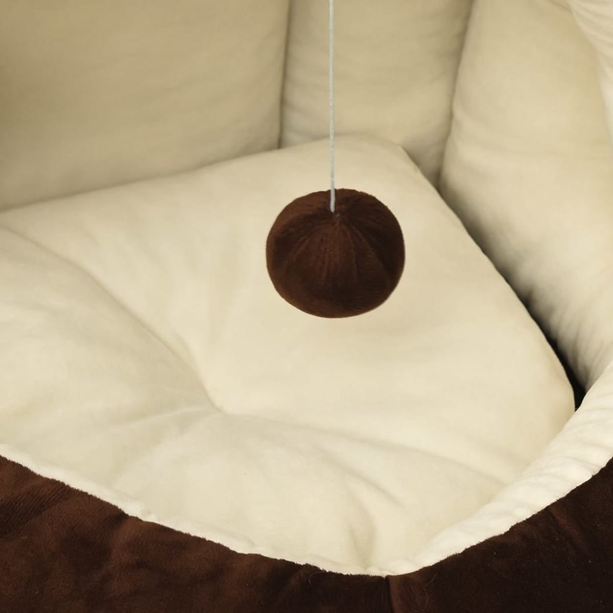 Ein brauner Ball hängt über einem weichen, weißen Haustierbett mit braunen Rändern. Der Hintergrund ist ein weiches, weißes Haustierbett.
