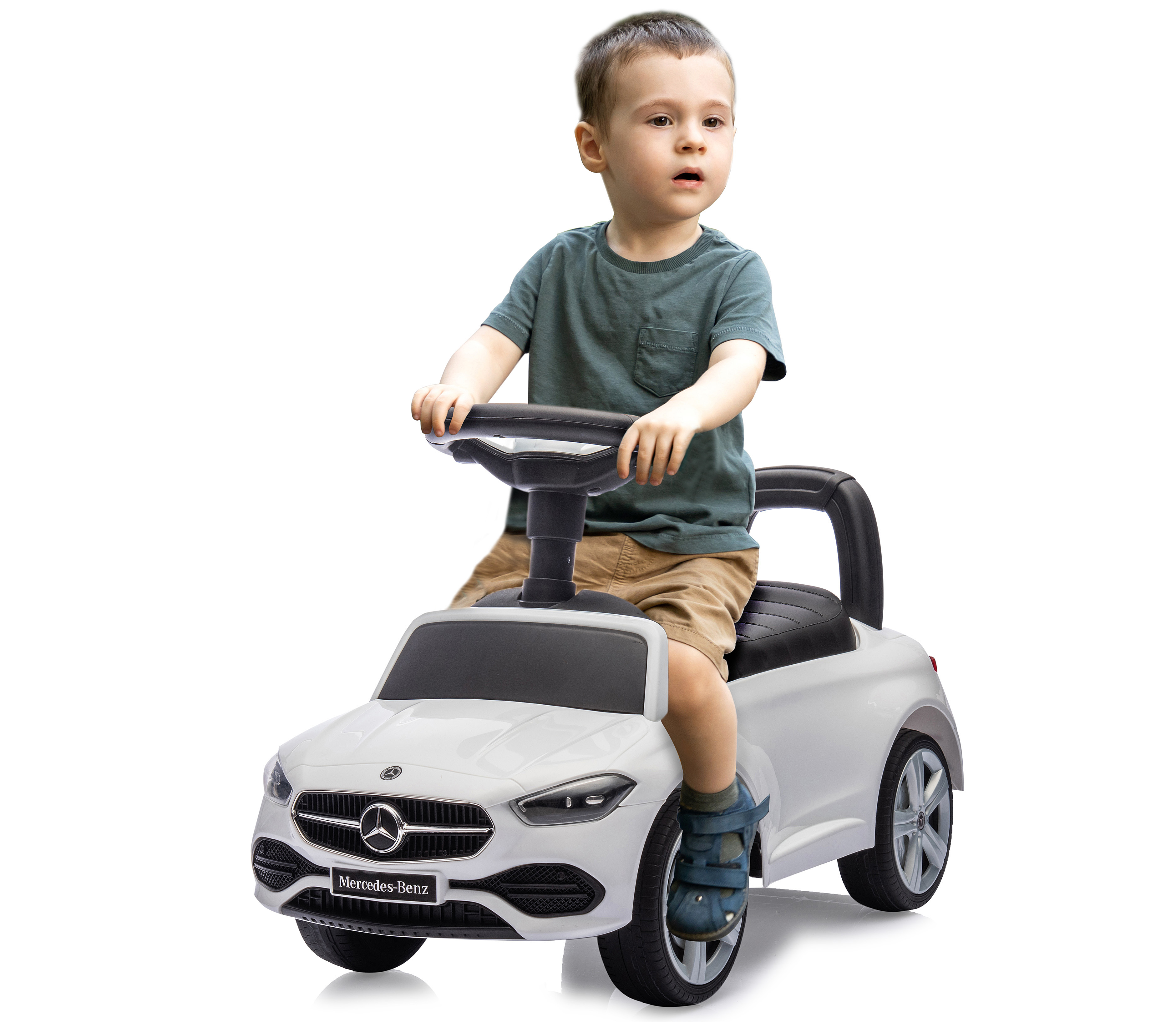 Ein kleiner Junge sitzt auf einem weißen Mercedes-Benz-Spielzeugauto und hält das Lenkrad. Er schaut zur Seite.