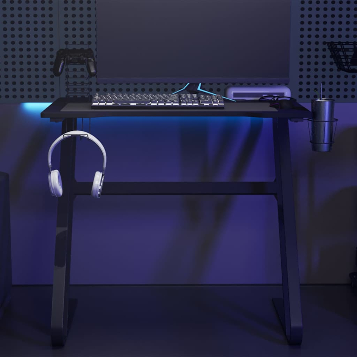 Gaming-Schreibtisch mit Tastatur, Headset, Monitor und Zubehör. Schwarzer Rahmen, blaue LED-Beleuchtung und ein Controller an der Wand.