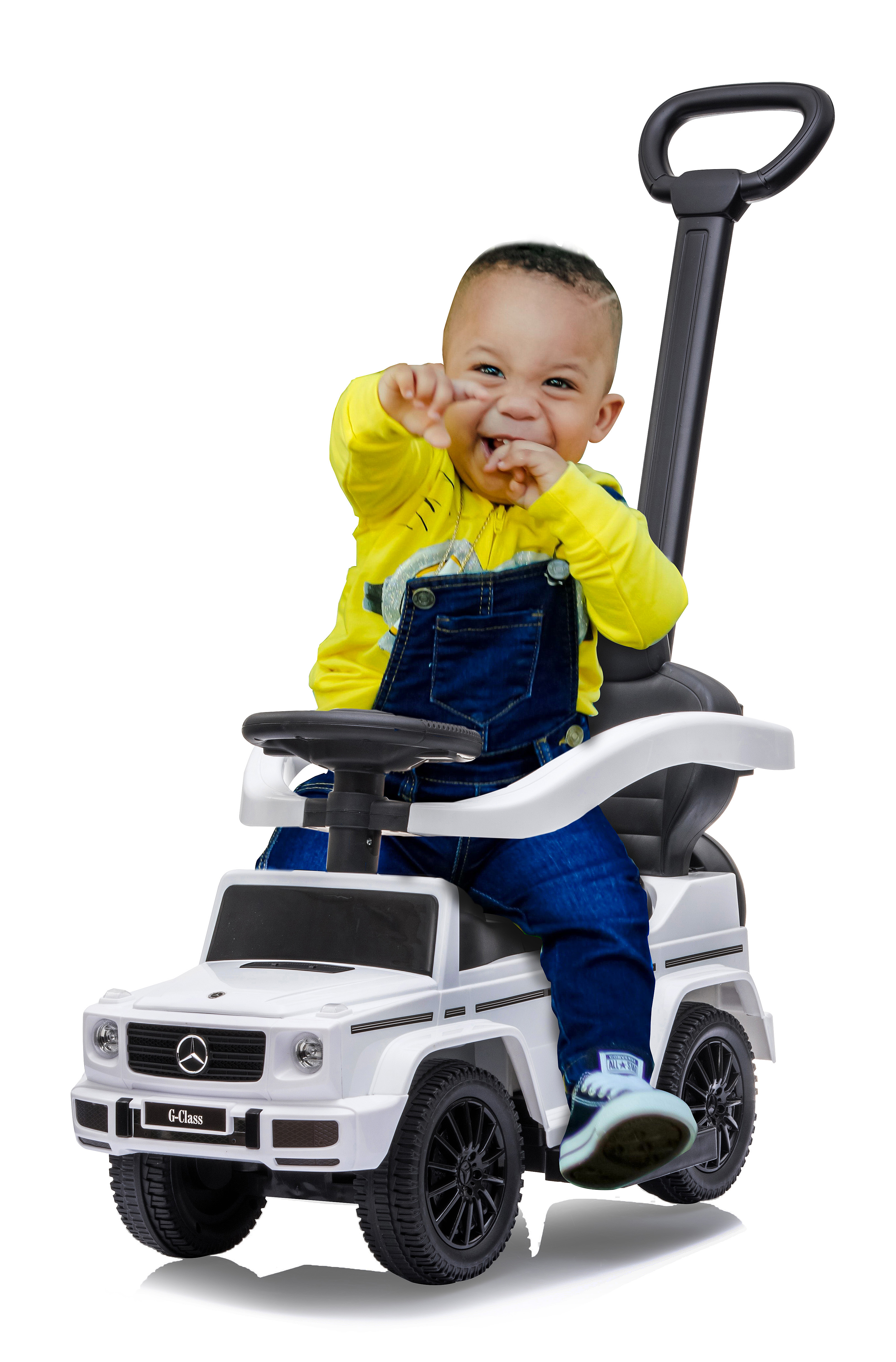 Un bambino sorridente con una maglietta gialla e una tuta blu è seduto su un'auto giocattolo bianca, facendo un gesto giocoso.