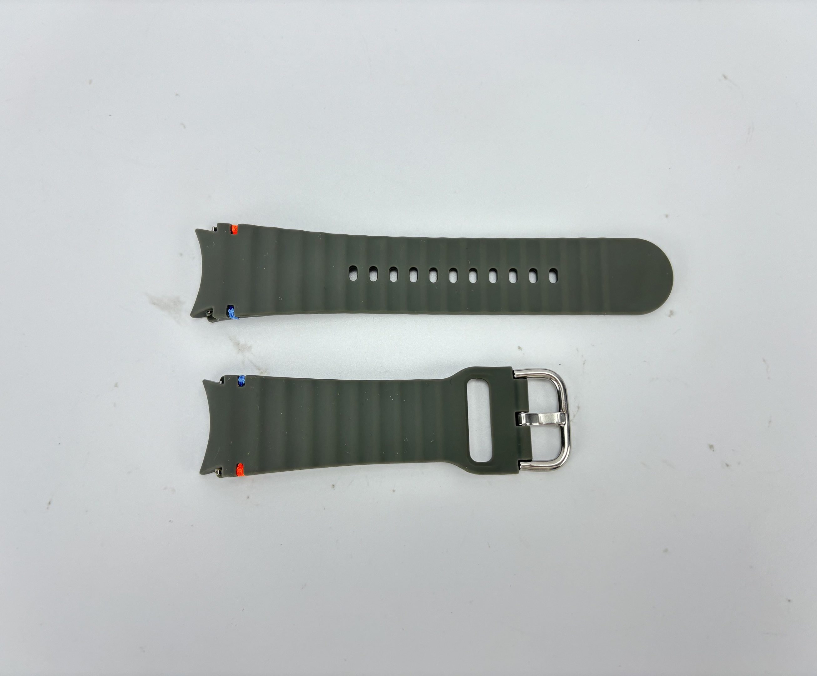 Zwei olivgrüne Uhrenarmbänder auf weißem Untergrund. Eines hat Löcher, das andere eine Schnalle.
