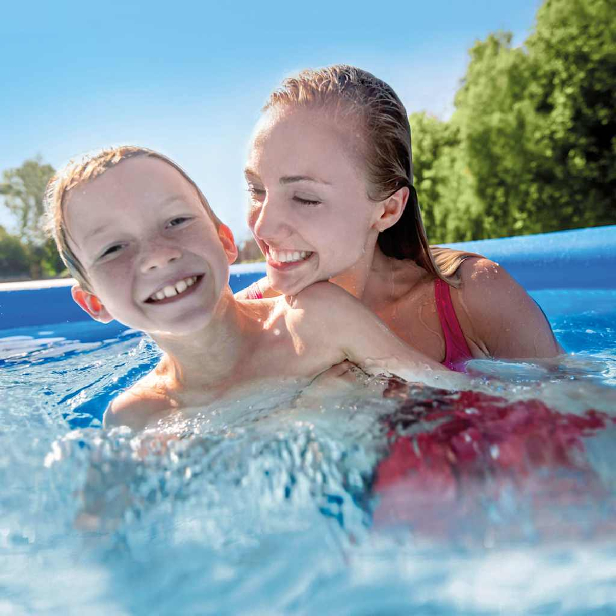 Eine Frau und ein Junge lächeln in einem Pool. Die Frau trägt ein rosafarbenes Oberteil. Blaues Poolwasser und grüne Bäume im Hintergrund.