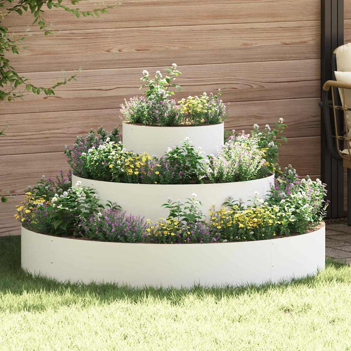 Una fioriera bianca a più livelli piena di fiori colorati è sull'erba. Una staccionata di legno e una sedia sullo sfondo.
