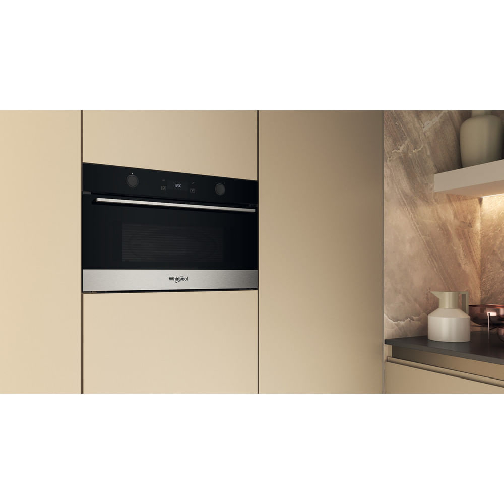 Cucina moderna con forno nero a incasso con pannello in acciaio inox e logo Whirlpool. Mobili beige circondano il forno.