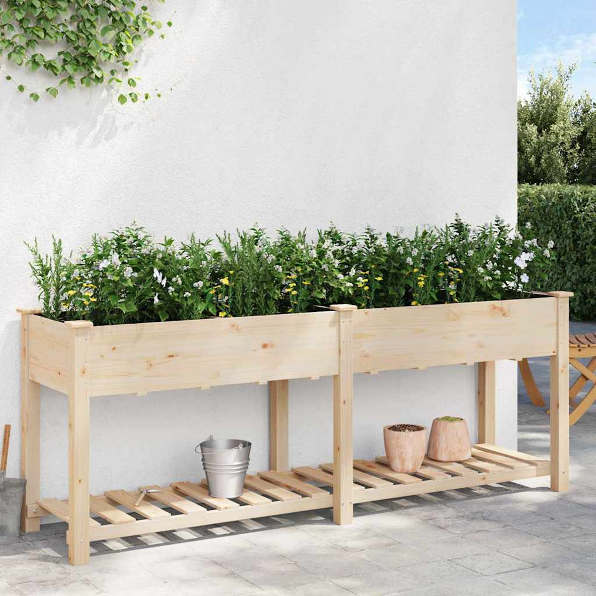 Fioriera in legno con piante. Un secchio di metallo e due vasi sullo scaffale inferiore. Un muro e piante sullo sfondo.