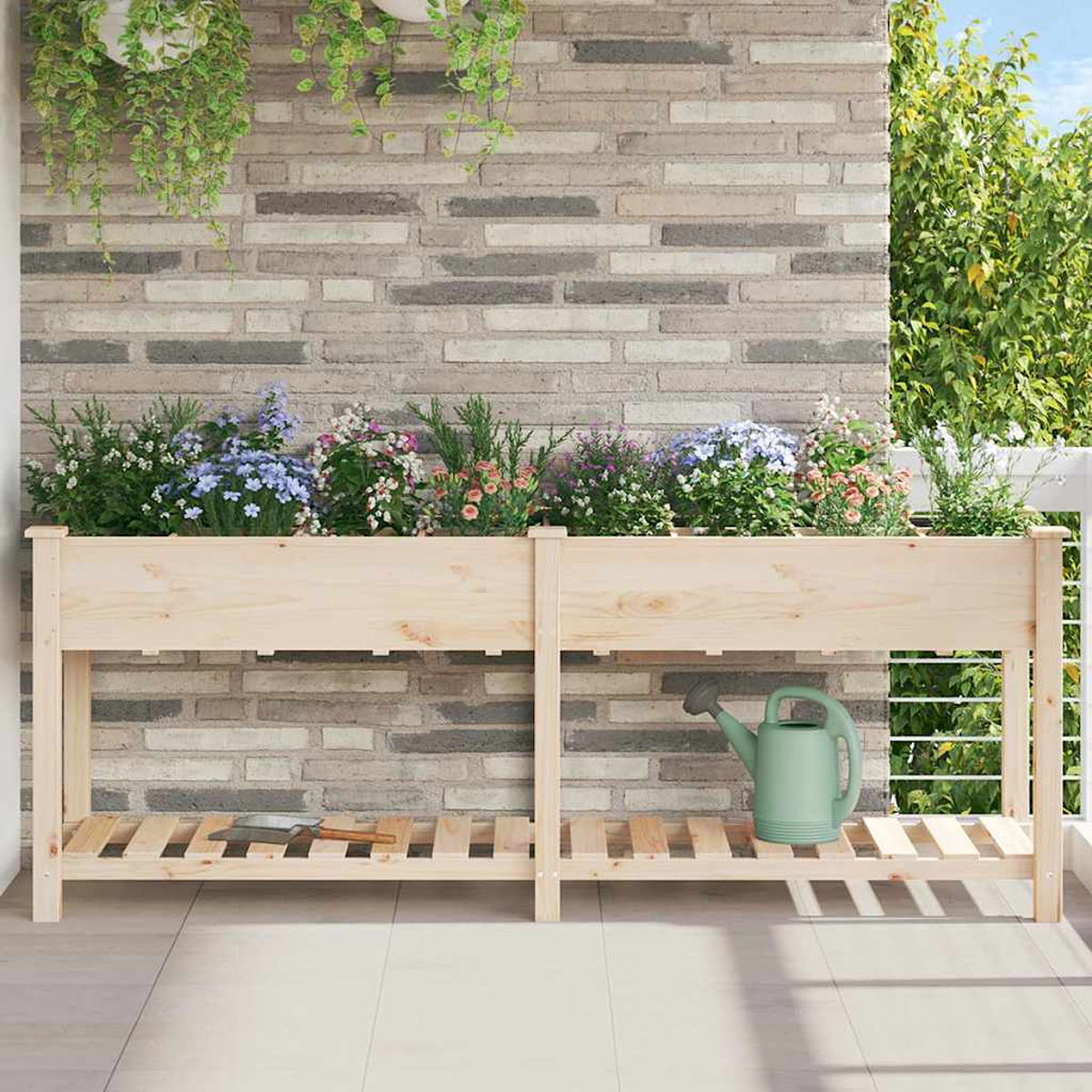 Fioriera in legno con fiori, un annaffiatoio e una cazzuola. Sfondo: muro di mattoni, piante e balcone.