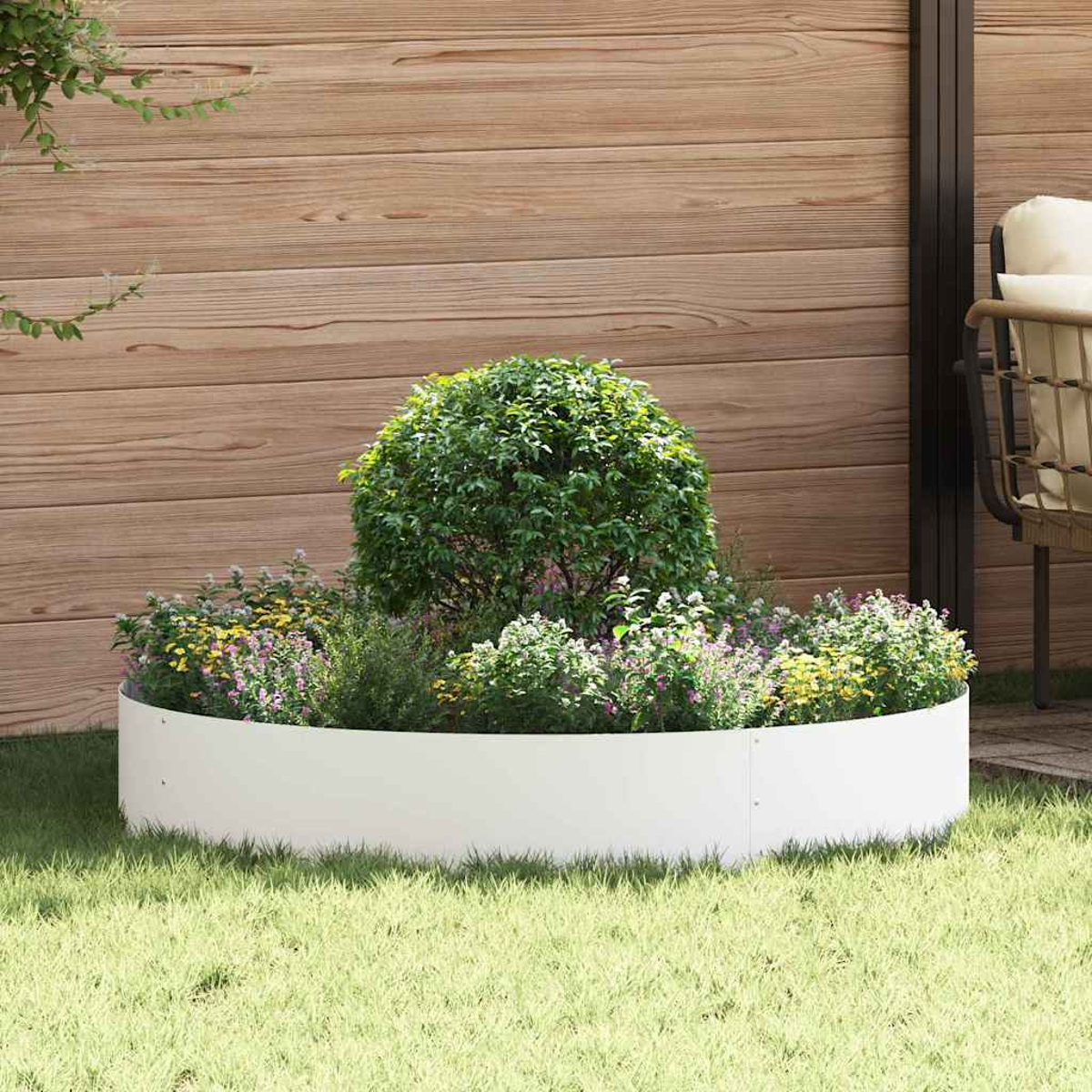 Un'aiuola rotonda è piena di piante e fiori. Si trova su un prato verde. Una recinzione di legno è sullo sfondo.