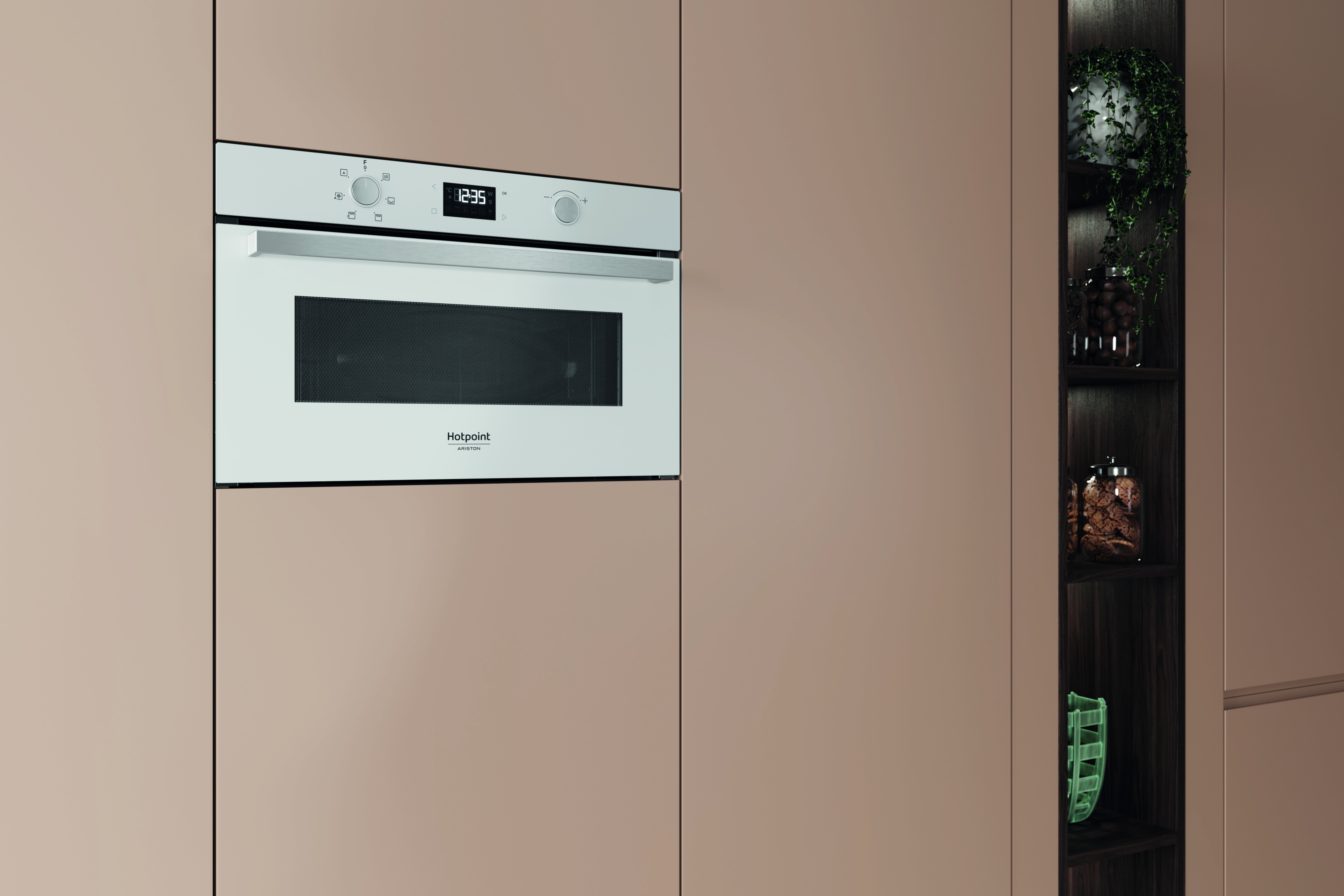 Un forno a microonde bianco con orologio digitale, integrato in un mobile da cucina color pesca, con un ripiano con piante e barattoli.
