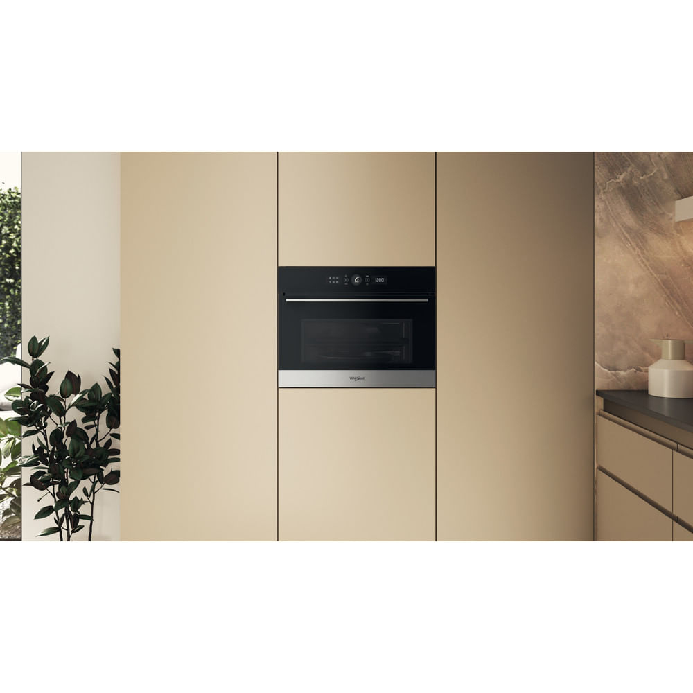 Un forno a microonde integrato è centrato in un mobile da cucina. Il mobile è beige chiaro. A sinistra c'è una pianta.
