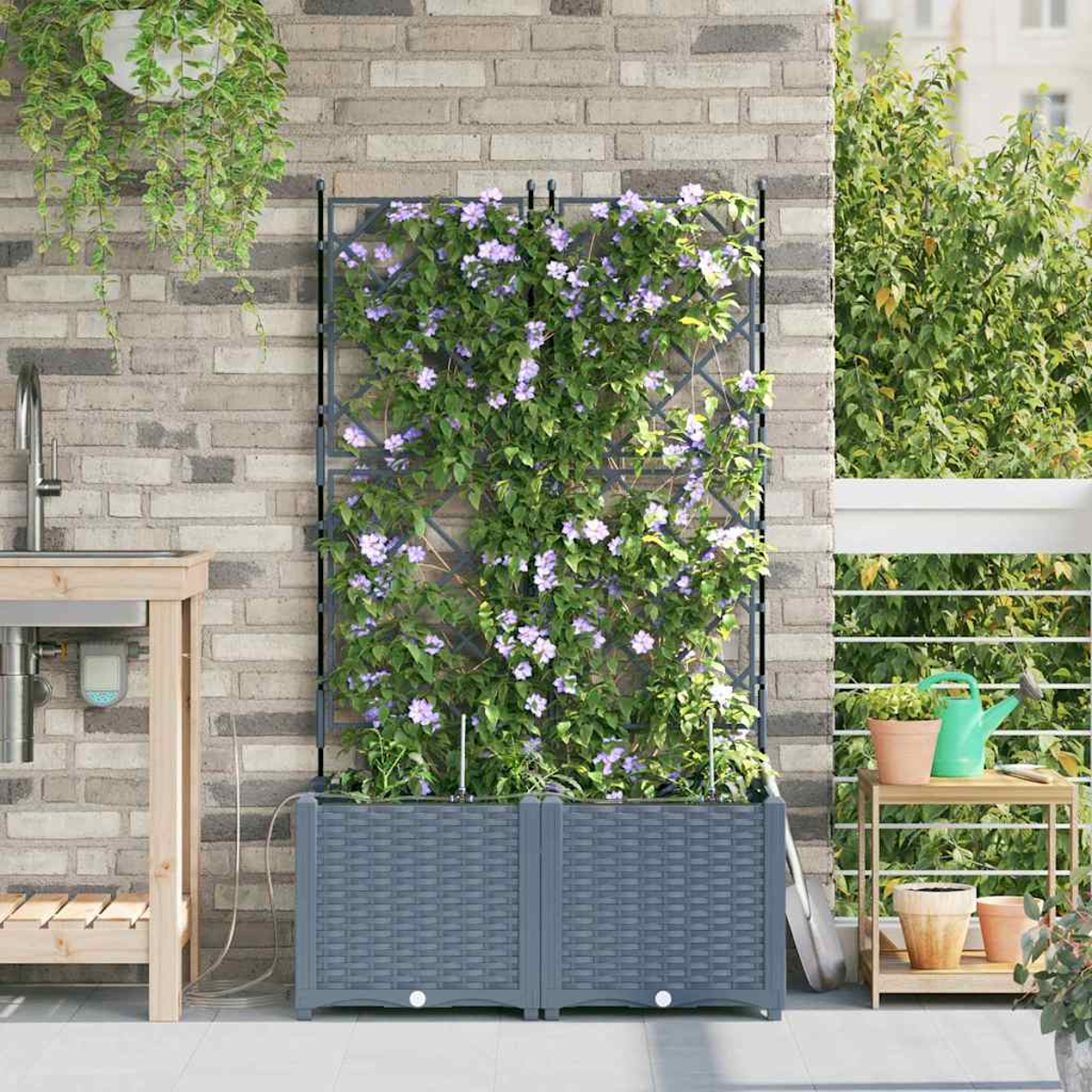 Un giardino sul balcone con fioriere grigie, piante rampicanti con fiori viola, un lavandino e un tavolino con piante.