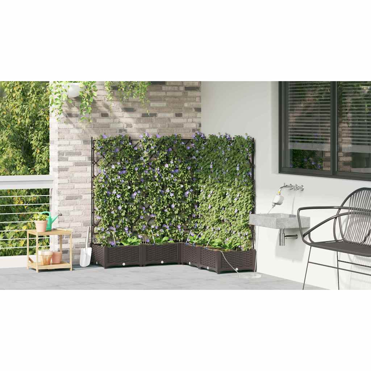 Una scena di patio presenta un muro verde con fiori viola, fioriere marroni, un lavandino, una sedia e un tavolino in legno con piante.