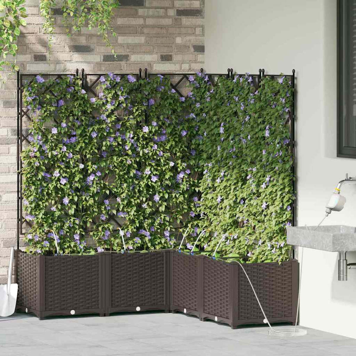 Ein brauner gewebter Pflanzer mit Kletterpflanzen, lila Blumen und einem Metallgitter. Eine weiße Schaufel lehnt daran. Ziegelmauer im Hintergrund.