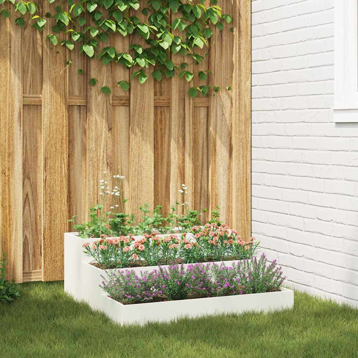 Una fioriera a più livelli con fiori si trova sull'erba. Una recinzione in legno e un muro di mattoni bianchi fanno da sfondo. Sono visibili viti e foglie verdi.