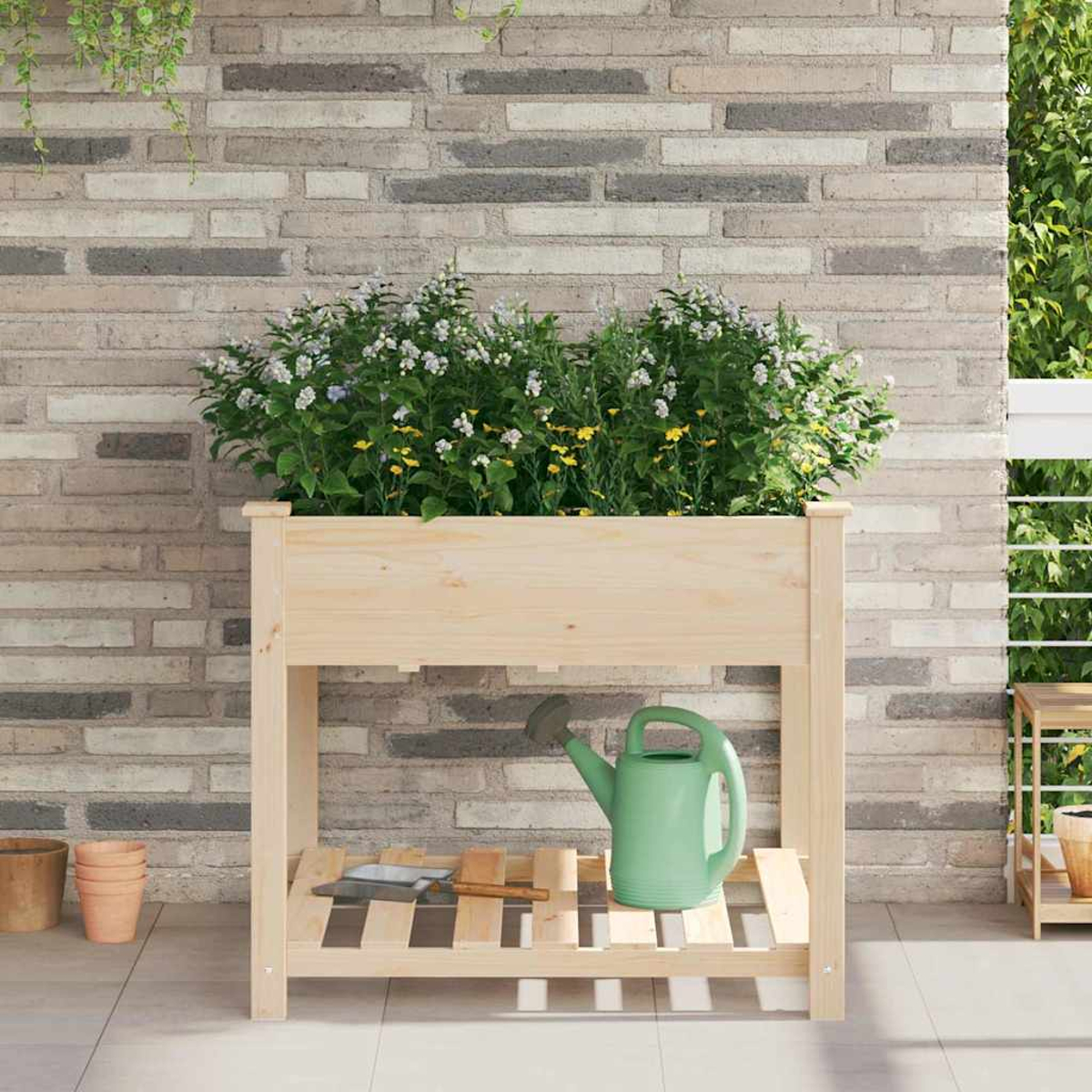 Fioriera in legno con fiori. Annaffiatoio verde sullo scaffale. Sfondo di muro di mattoni. Vasi a sinistra e a destra.