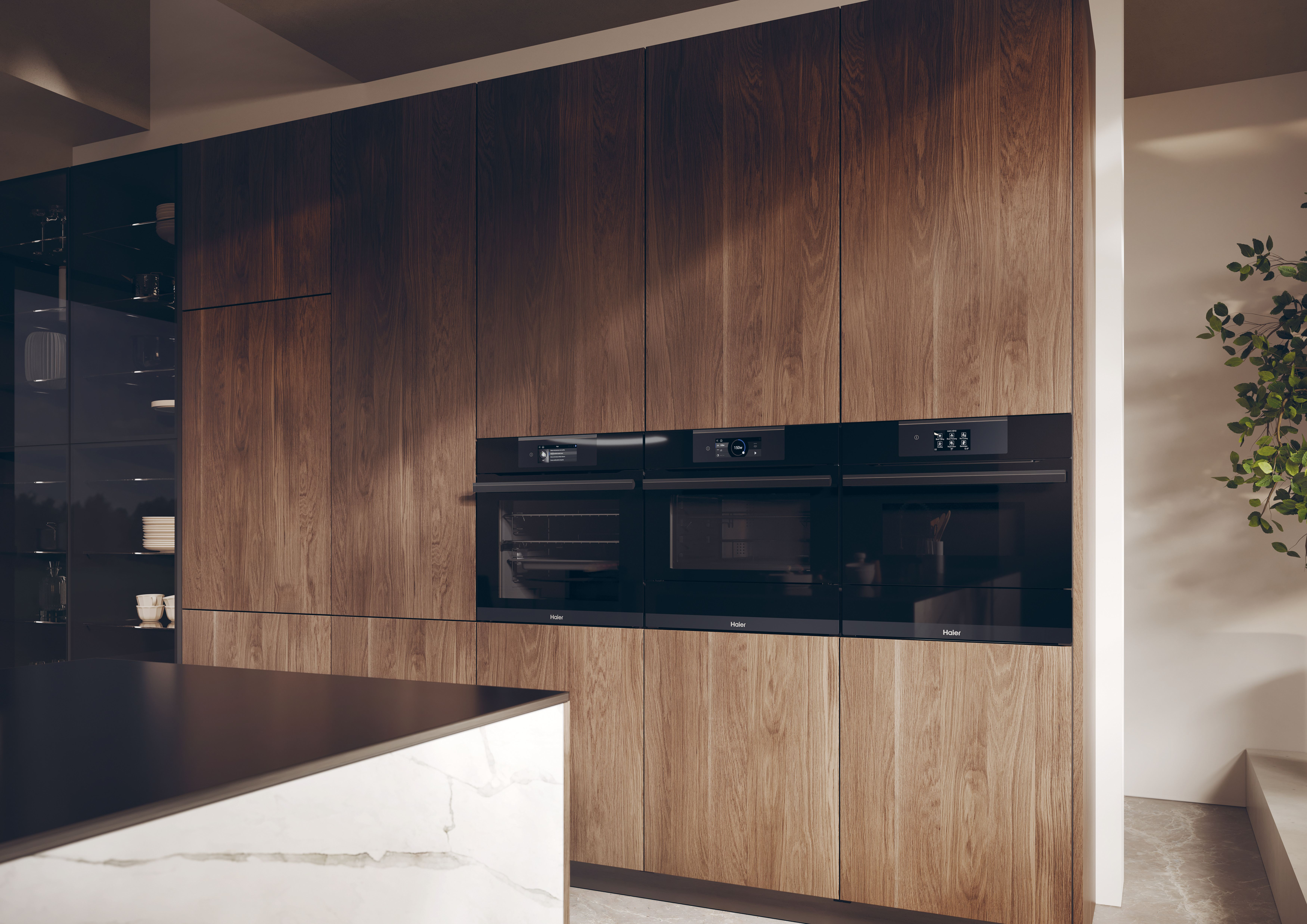 Cocina moderna con gabinetes de madera y hornos negros empotrados. También se ve una encimera de mármol y una planta.