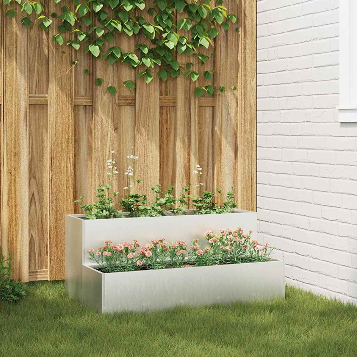 Una fioriera a due livelli con piante rosa e verdi si trova sull'erba. Una recinzione di legno e un muro di mattoni bianchi sono sullo sfondo.