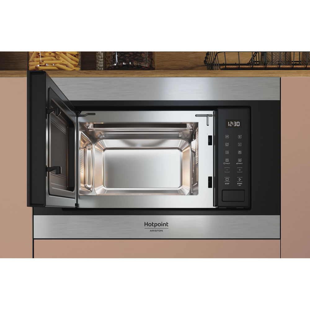 Een Hotpoint magnetron staat open. De binnenkant is glanzend en het bedieningspaneel toont 12:30. Pasta en koffiebonen op de achtergrond.