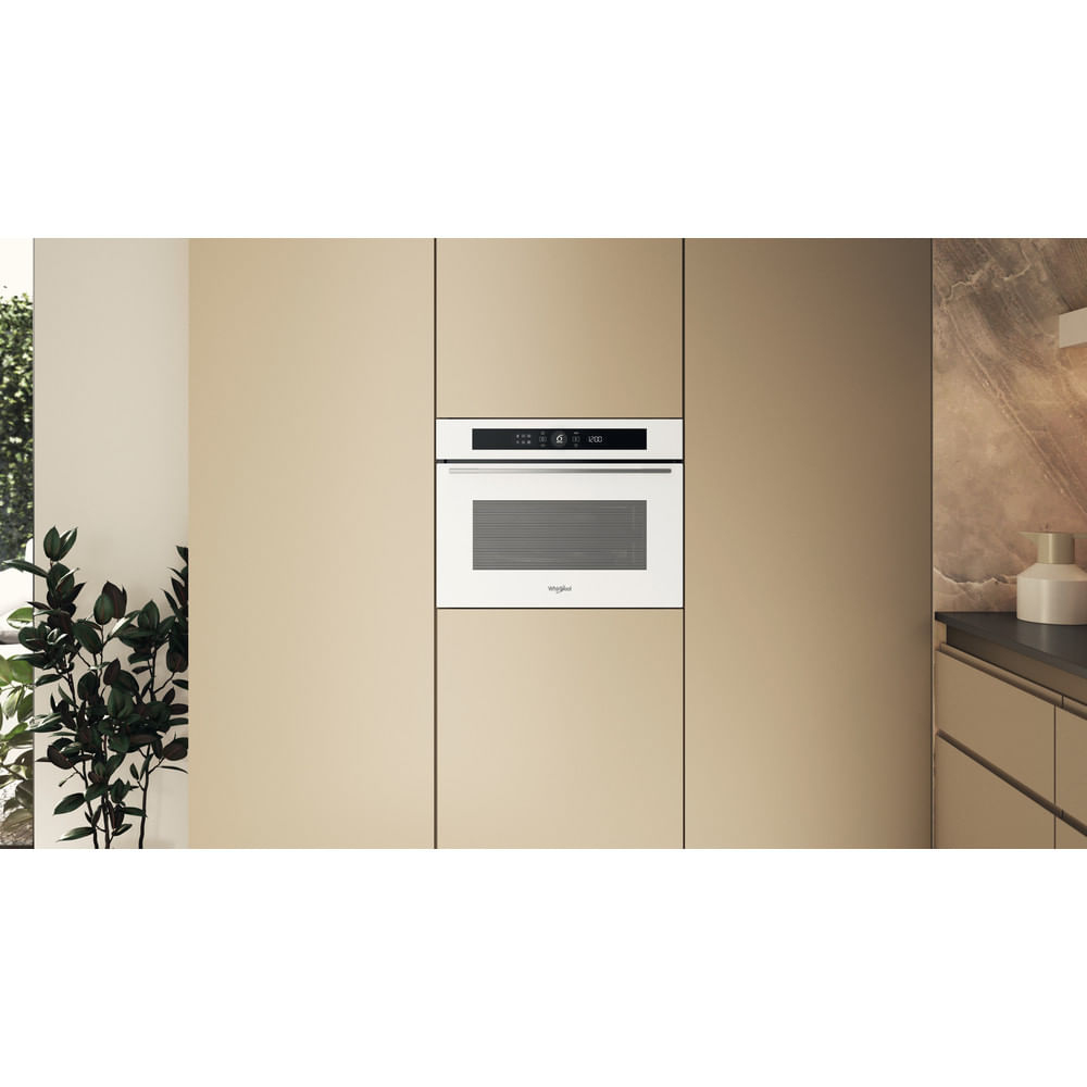 Un forno a microonde bianco integrato è al centro di una cucina. È circondato da armadi beige. Una pianta è visibile a sinistra.