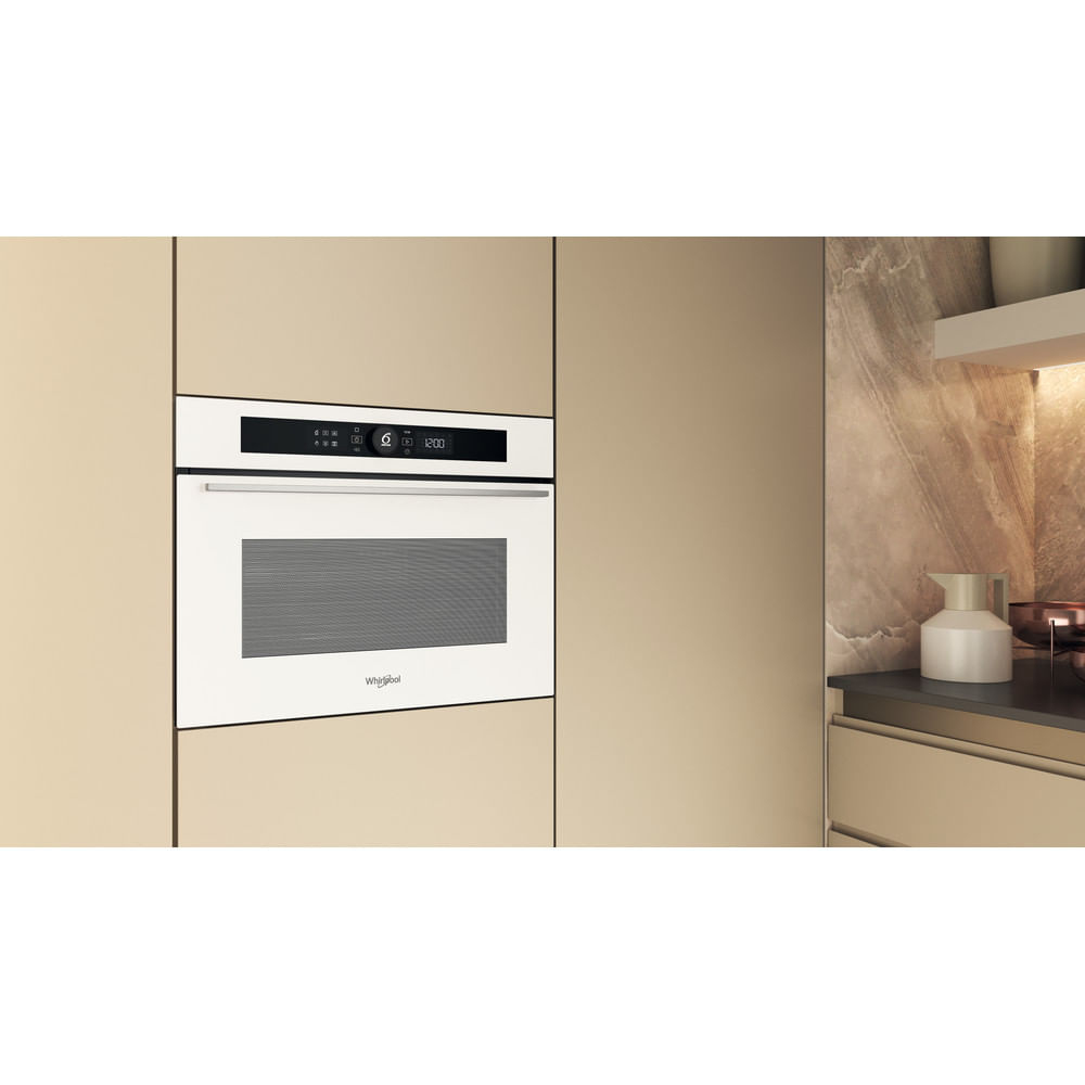 Un forno a microonde Whirlpool bianco è integrato in un mobile da cucina beige. Il forno mostra un orologio e i comandi. Una brocca è vicina.