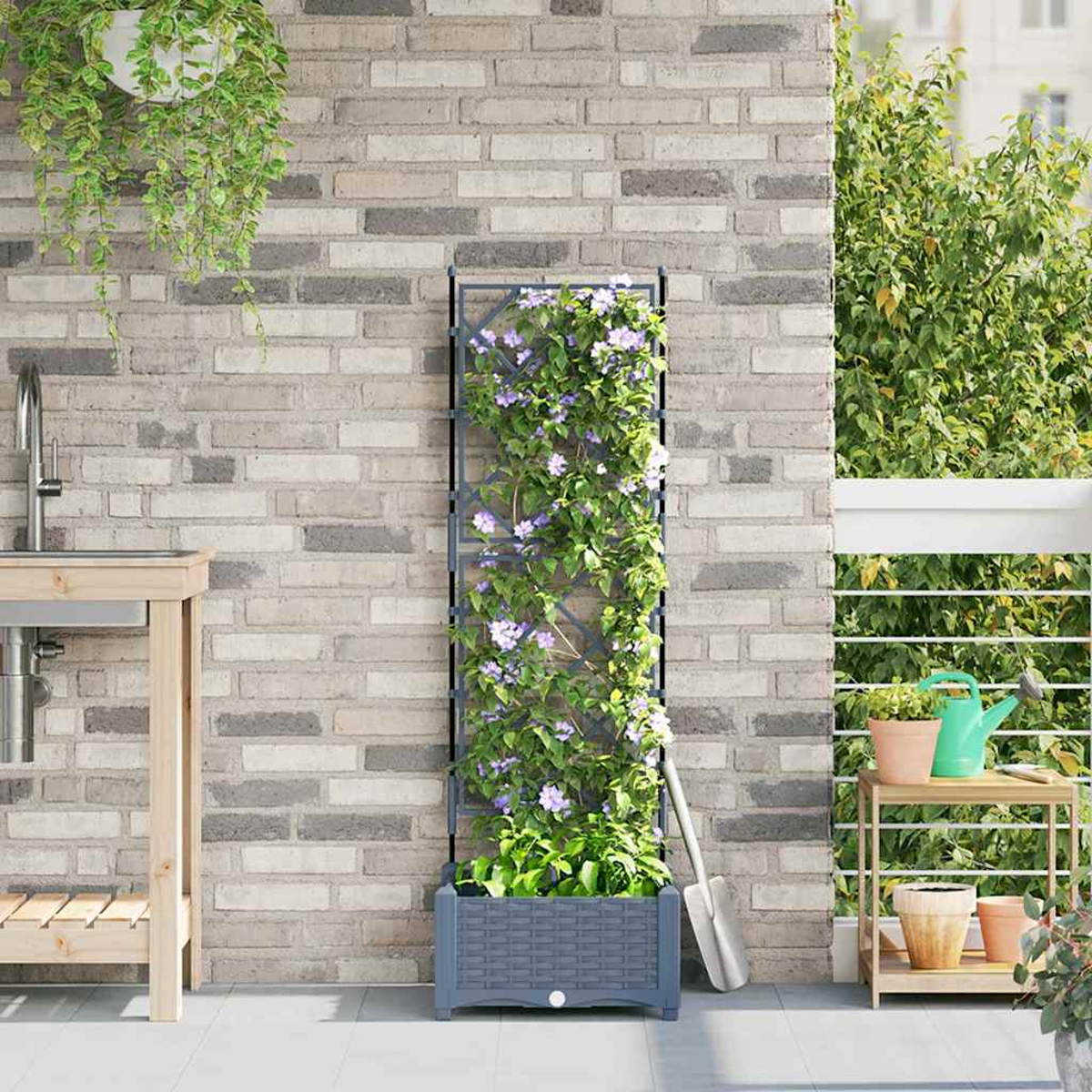 Un patio con un muro di mattoni grigi, un traliccio con fiori, un tavolo di legno con un lavandino e piante in vaso.